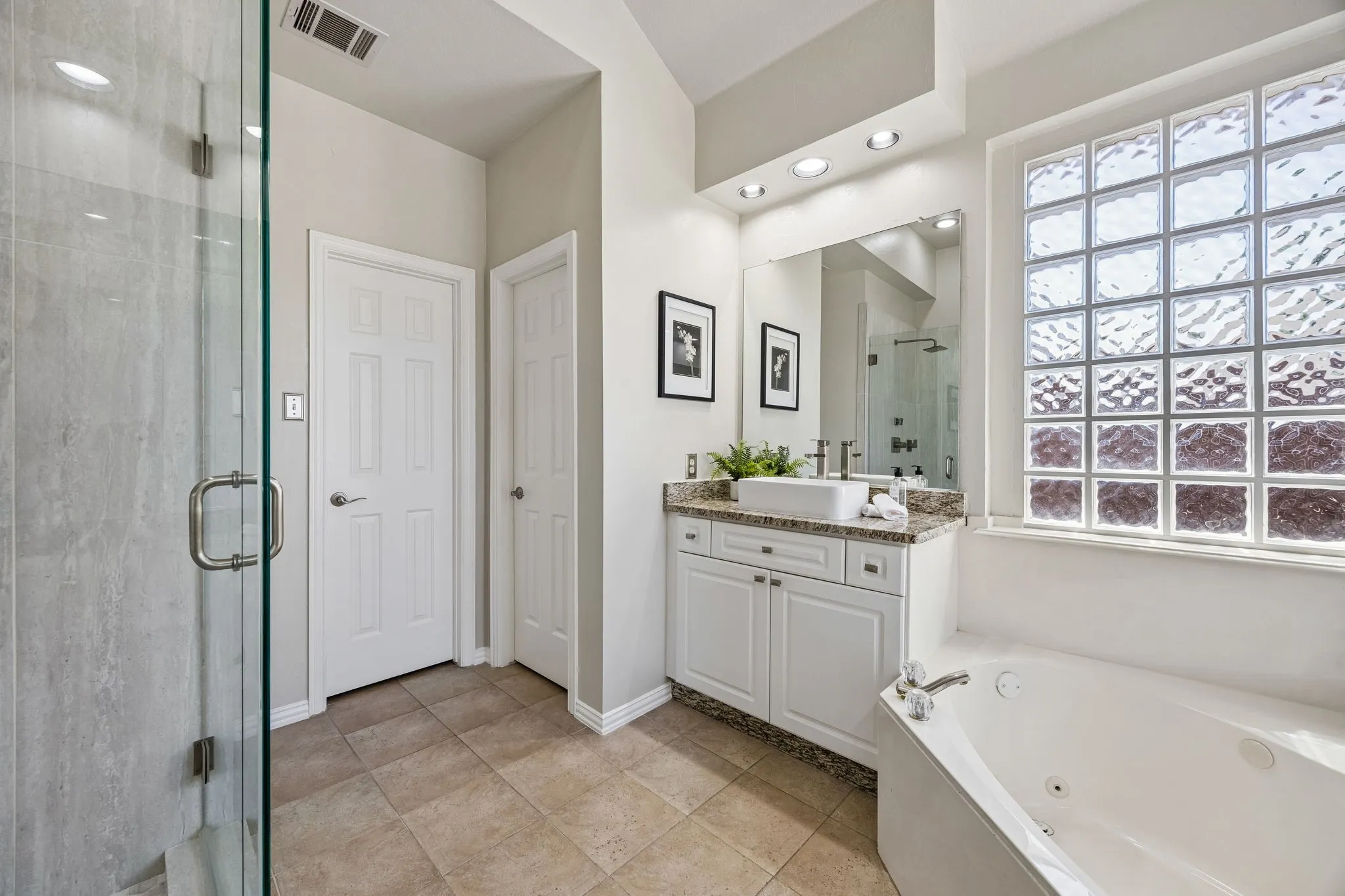 Glass-enclosed shower, jetted soaking tub, glass block window, double doors, and a vanity with a vessel sink