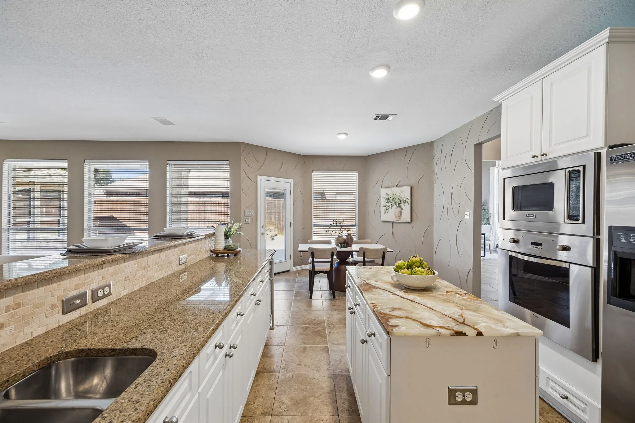 Kitchen featuring a double basin stainless steel sink, granite countertops with a stone tile backsplash, white cabinetry, and stainless steel appliances