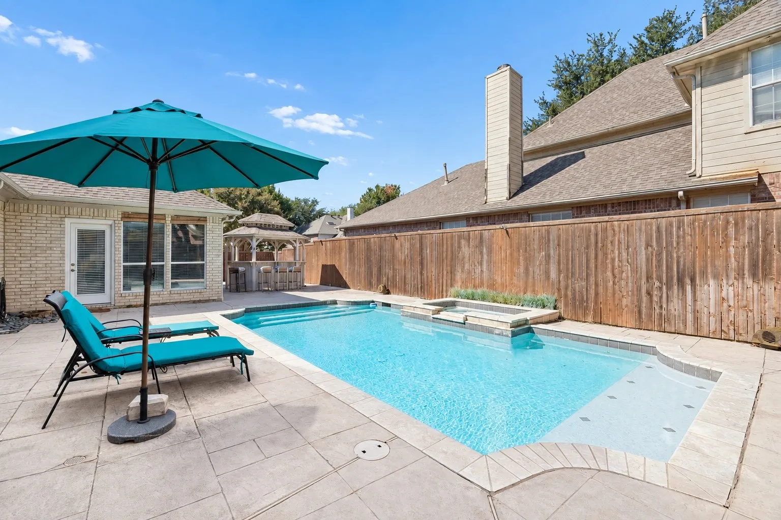 Pool with integrated spa, bordered by a concrete patio and privacy fencing