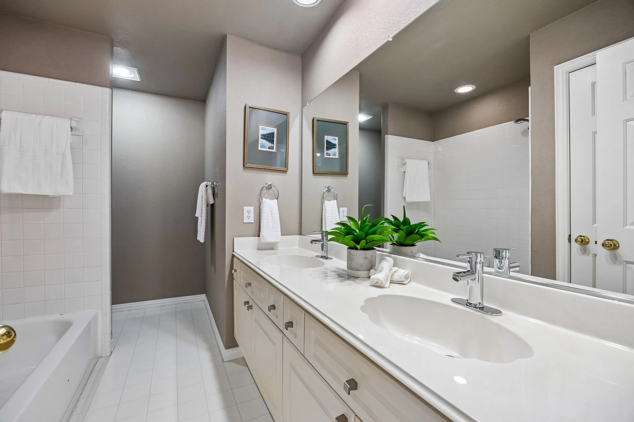 Dual vanity with integrated sinks, expansive mirror, white tile flooring, and white tiled tub surround