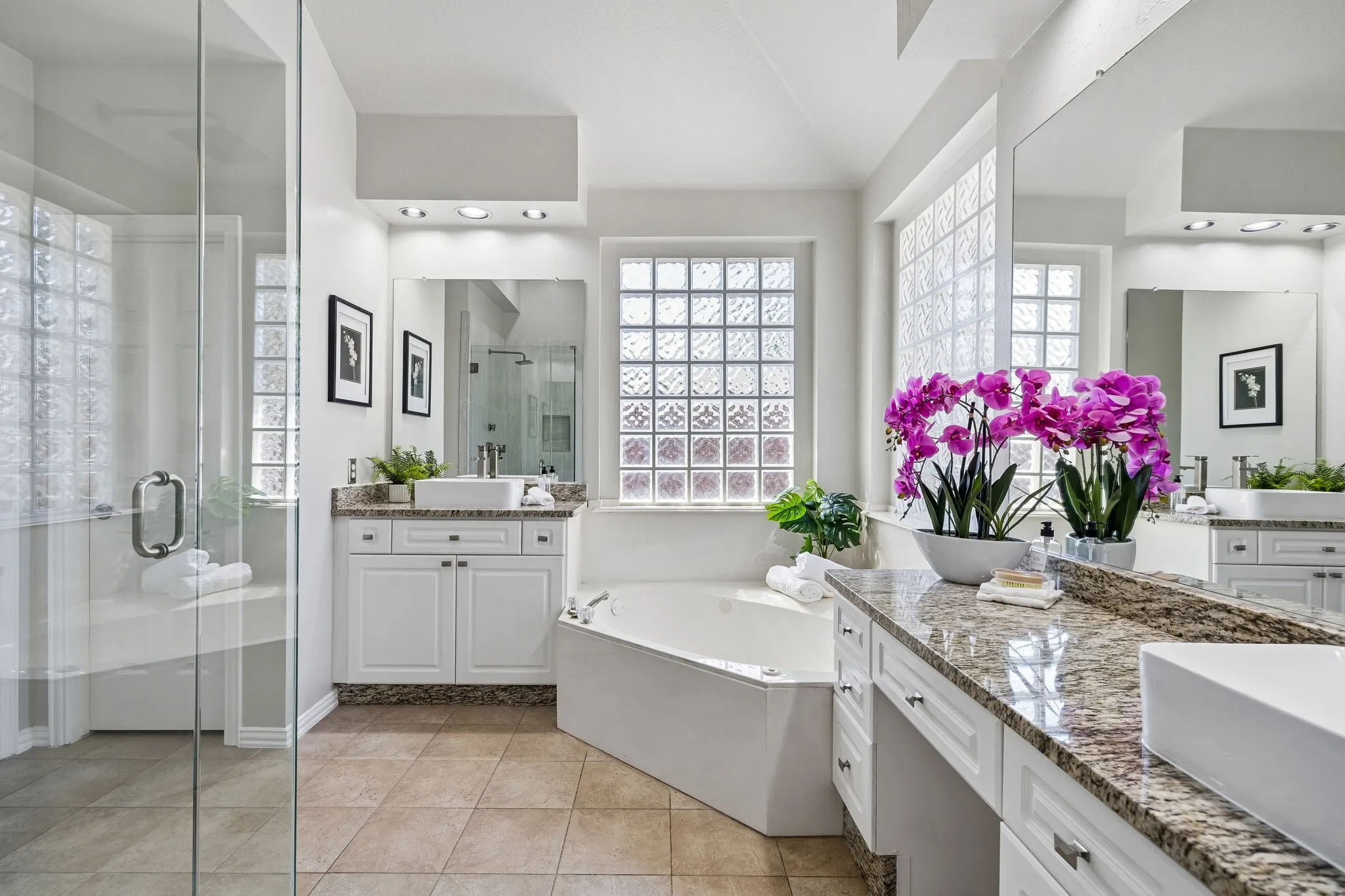 Glass-enclosed shower with a built-in bench, corner soaking tub, dual vanity with granite countertops, and tile flooring