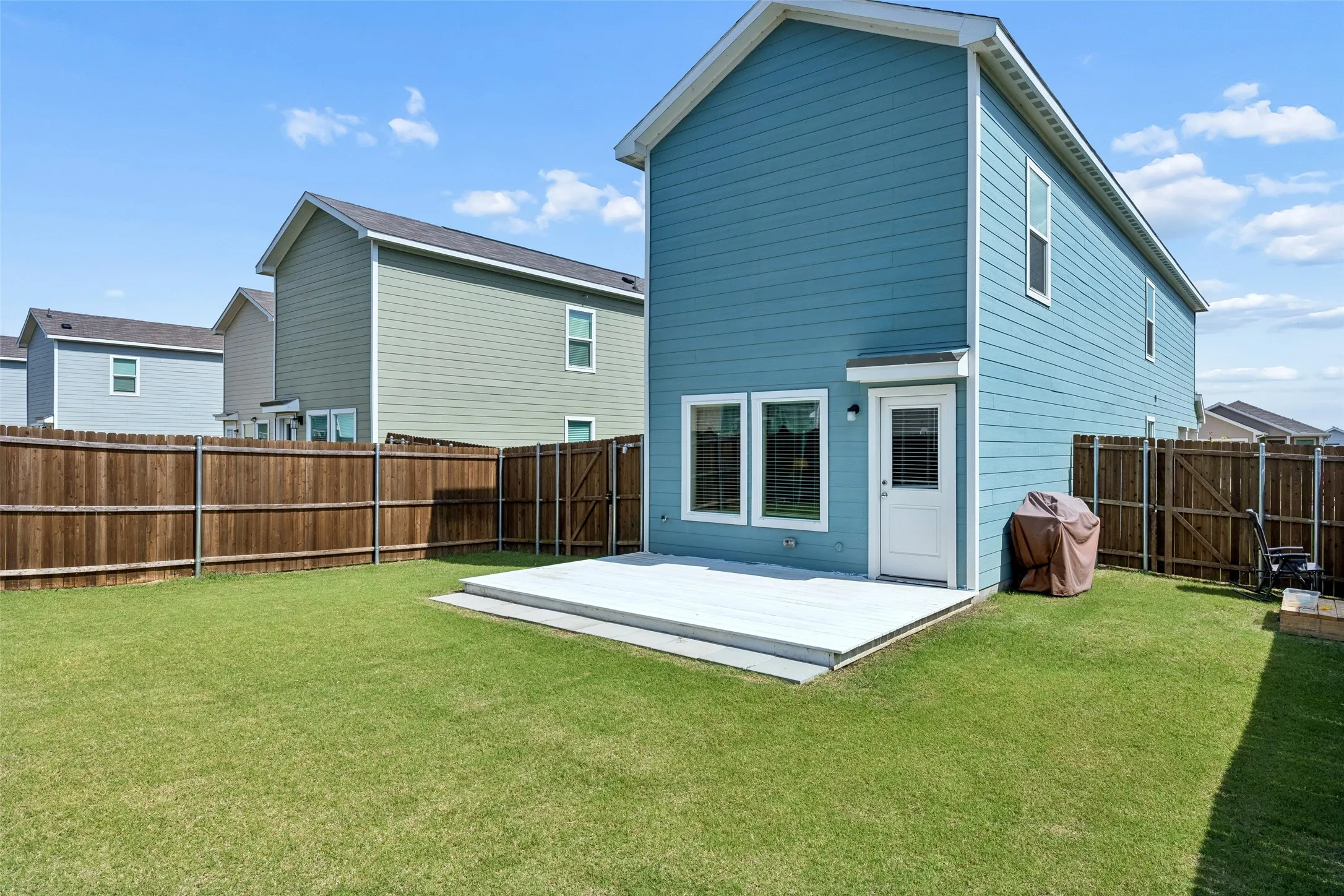 Expansive green lawn, wood privacy fencing, a white deck, and a white exterior door with glass insert