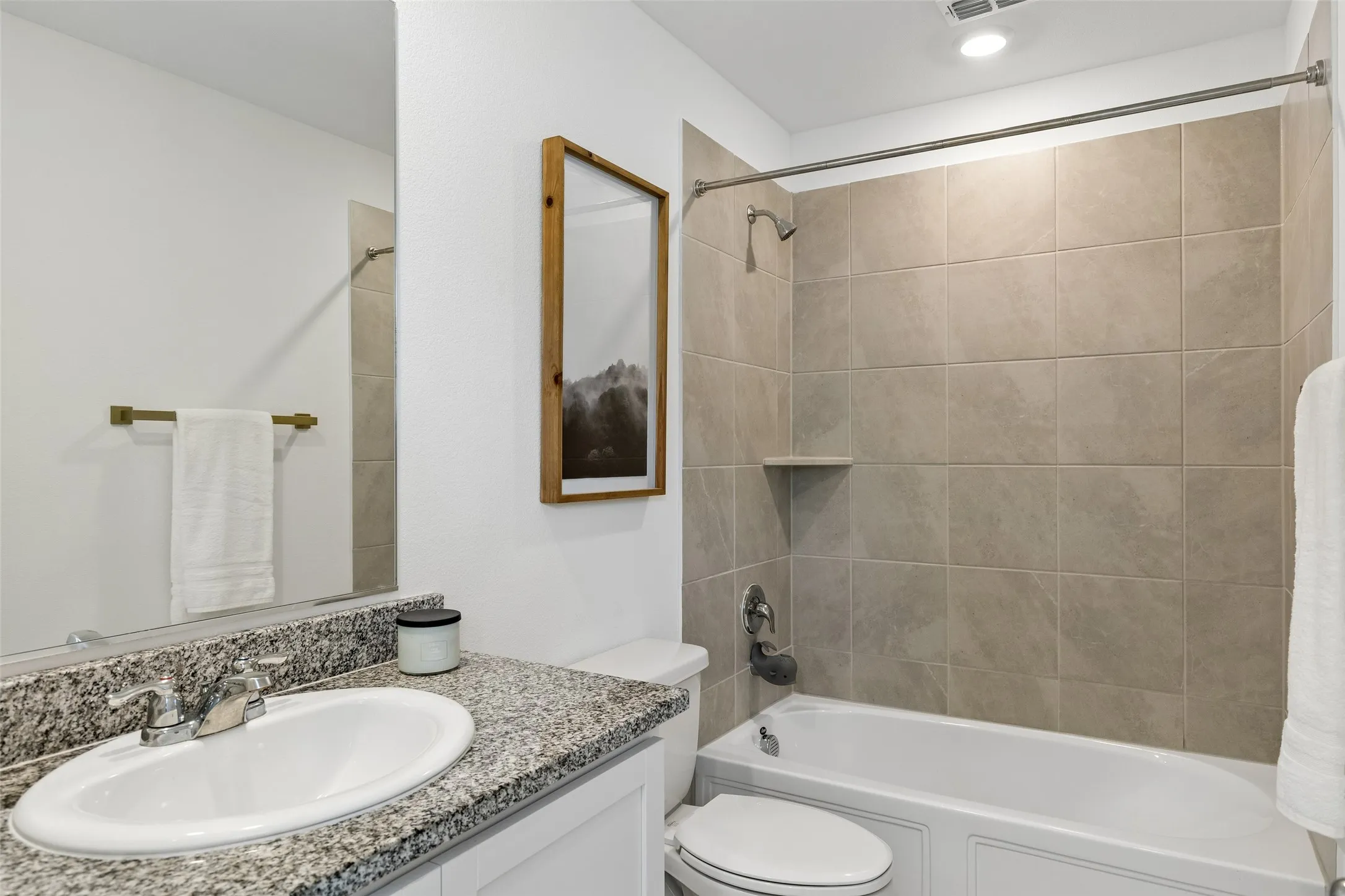 White vanity with granite-style countertop and integrated sink, full-width mirror, and a tiled shower-over-tub with a built-in niche