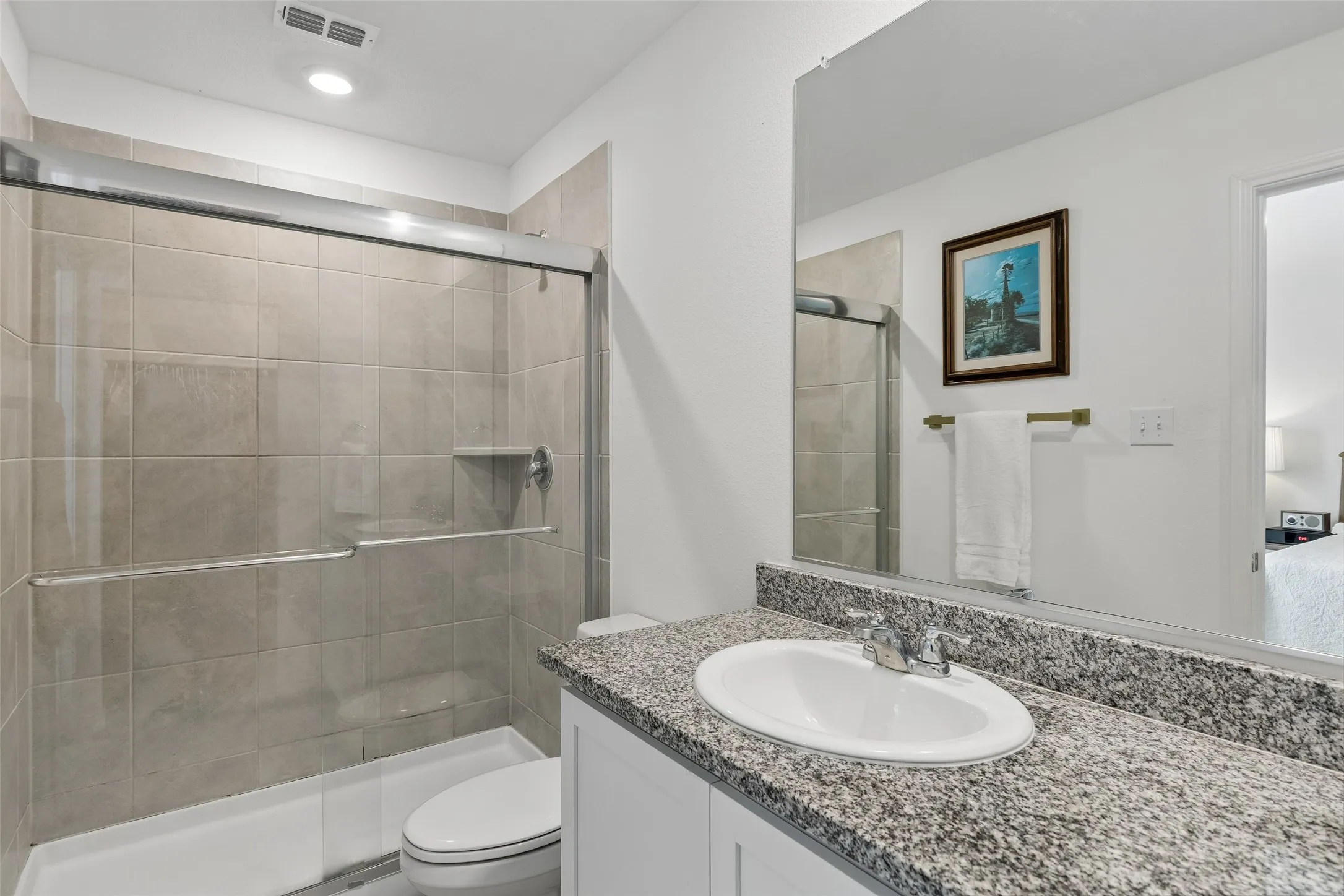 Bathroom featuring a sliding glass shower enclosure, tiled shower surround, built-in shower niche, and a vanity with a stone-finish countertop and integrated sink