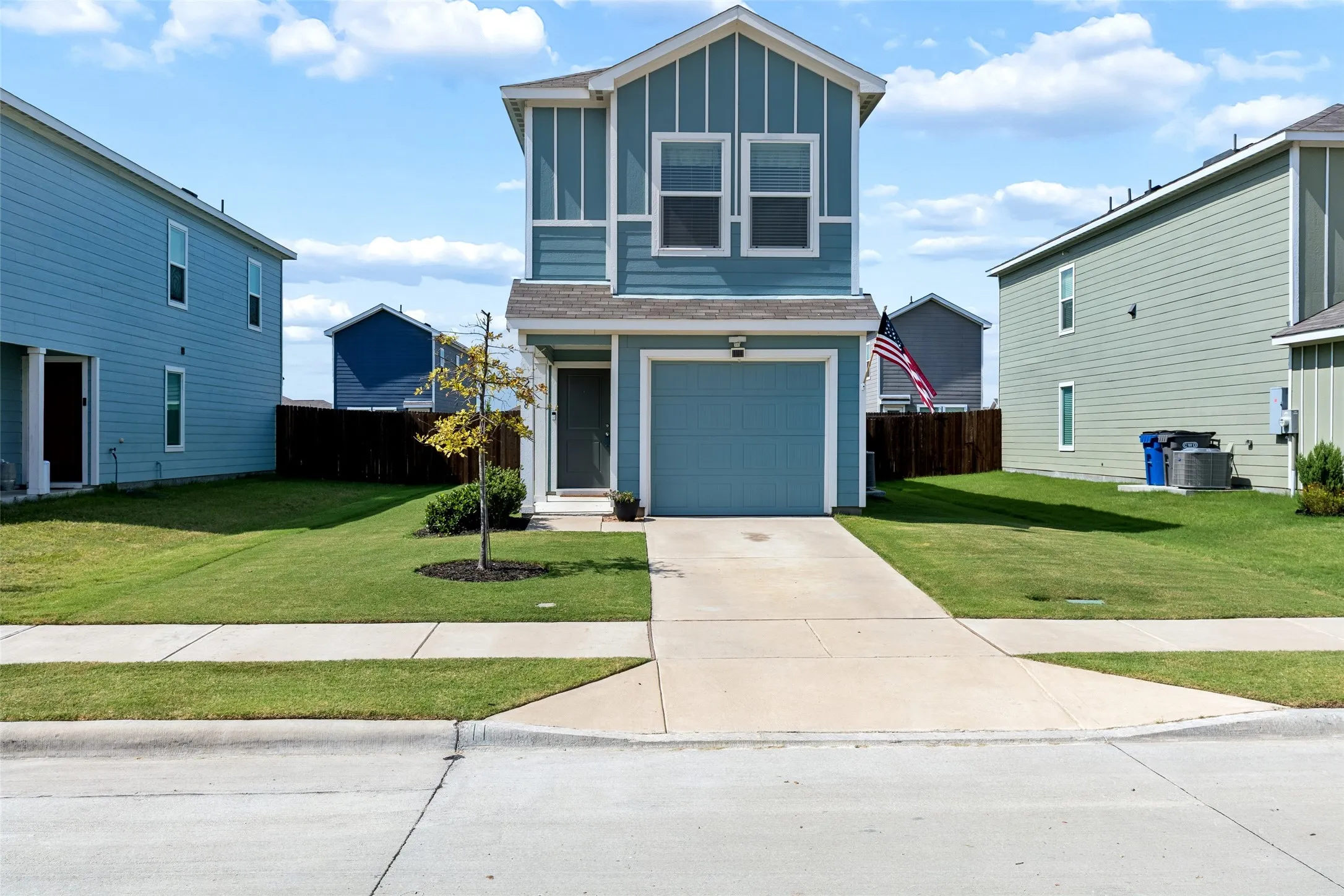 Two-story exterior with vertical and horizontal siding, an attached garage, a concrete driveway, and a manicured lawn