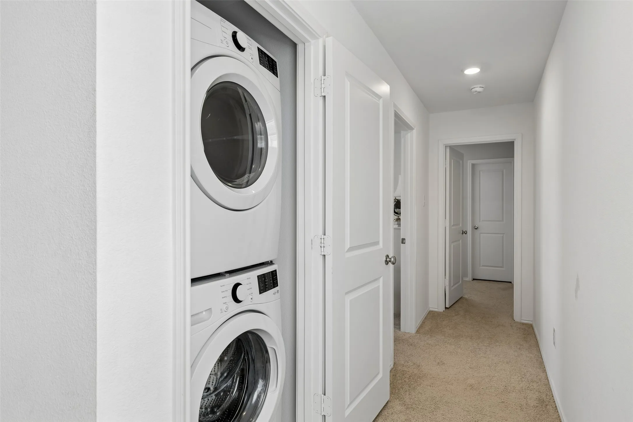 Stackable laundry appliances with front-loading washer and dryer, recessed lighting, and neutral carpeting