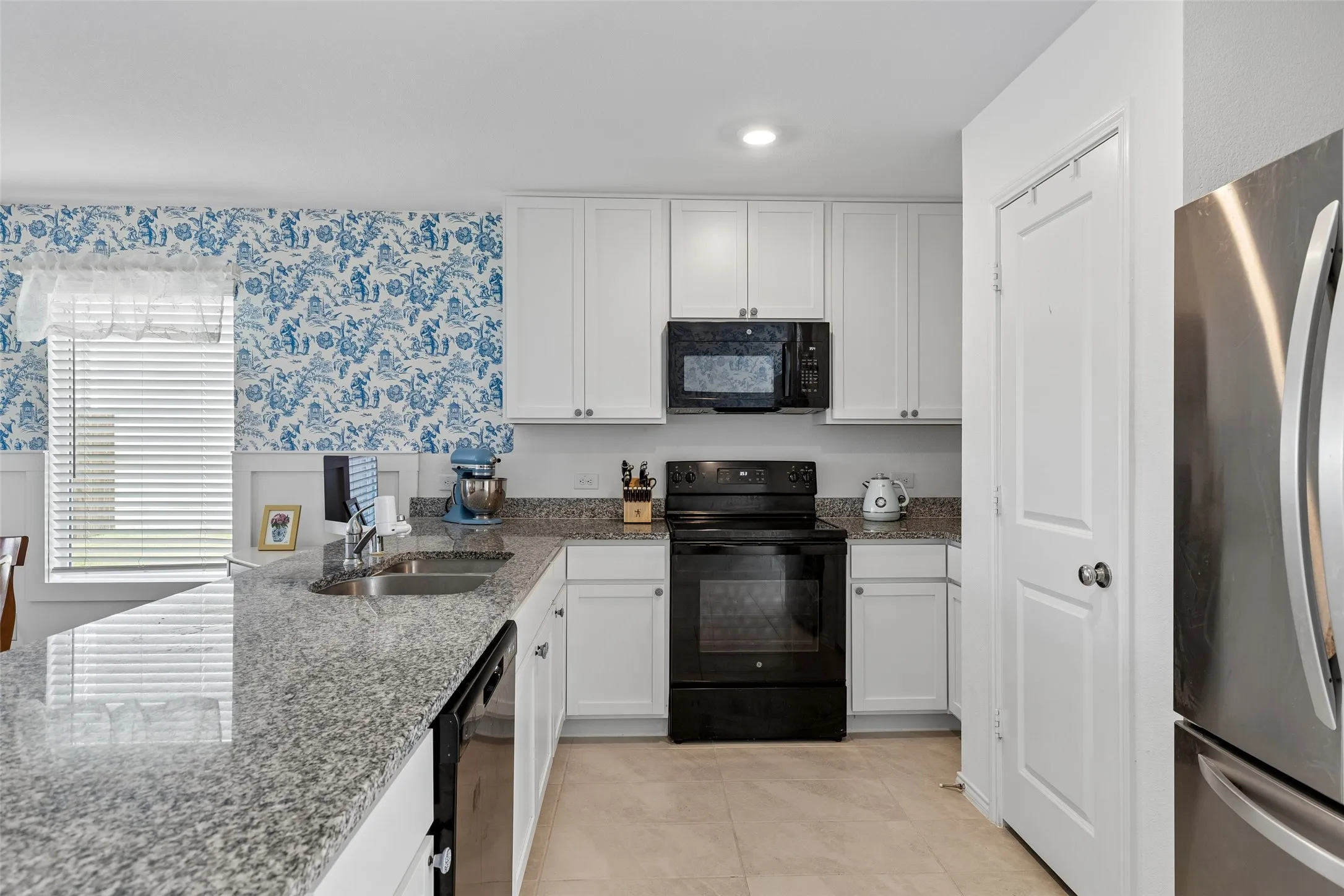 White cabinetry, granite countertops, appliances, and tile flooring