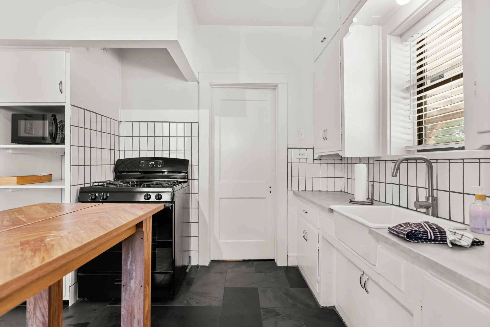 Kitchen with dark tile flooring, white subway tile backsplash, white cabinetry, a black range, and a white farmhouse sink with a gooseneck faucet
