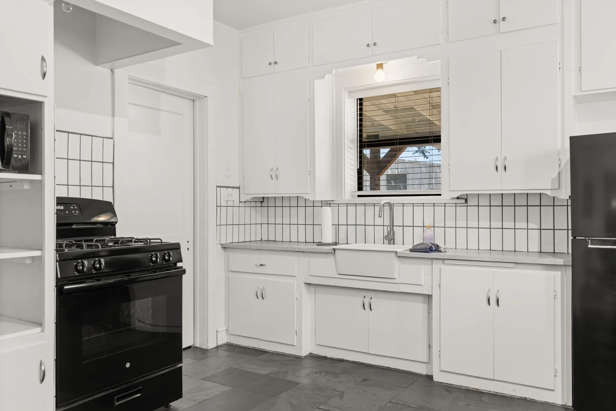 White cabinetry, tile backsplash, built-in shelving, black appliances, and durable flooring