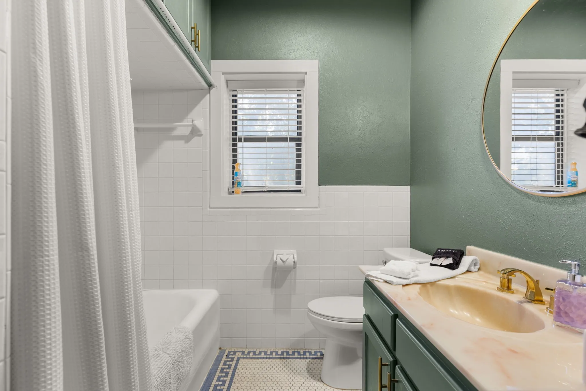Bathroom featuring a vanity with a counter and integrated sink, a built-in bathtub with a shower, a window with blinds, and hexagon tile flooring with a patterned border