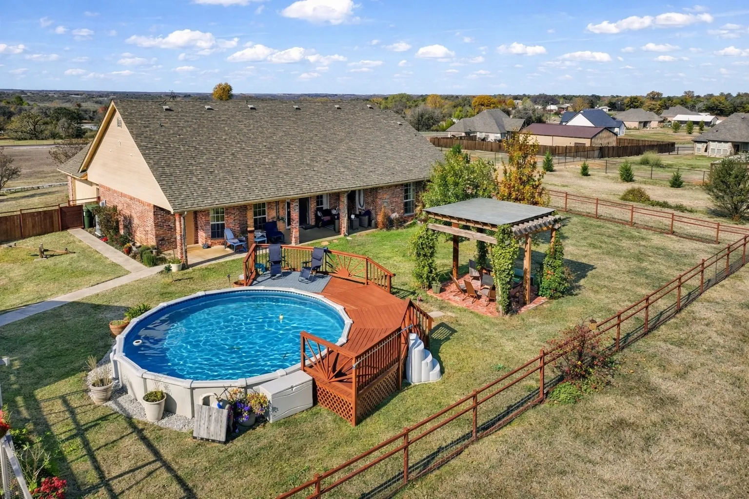 Brick exterior, gabled roof, above-ground pool with wood deck, covered pergola, and fenced yard