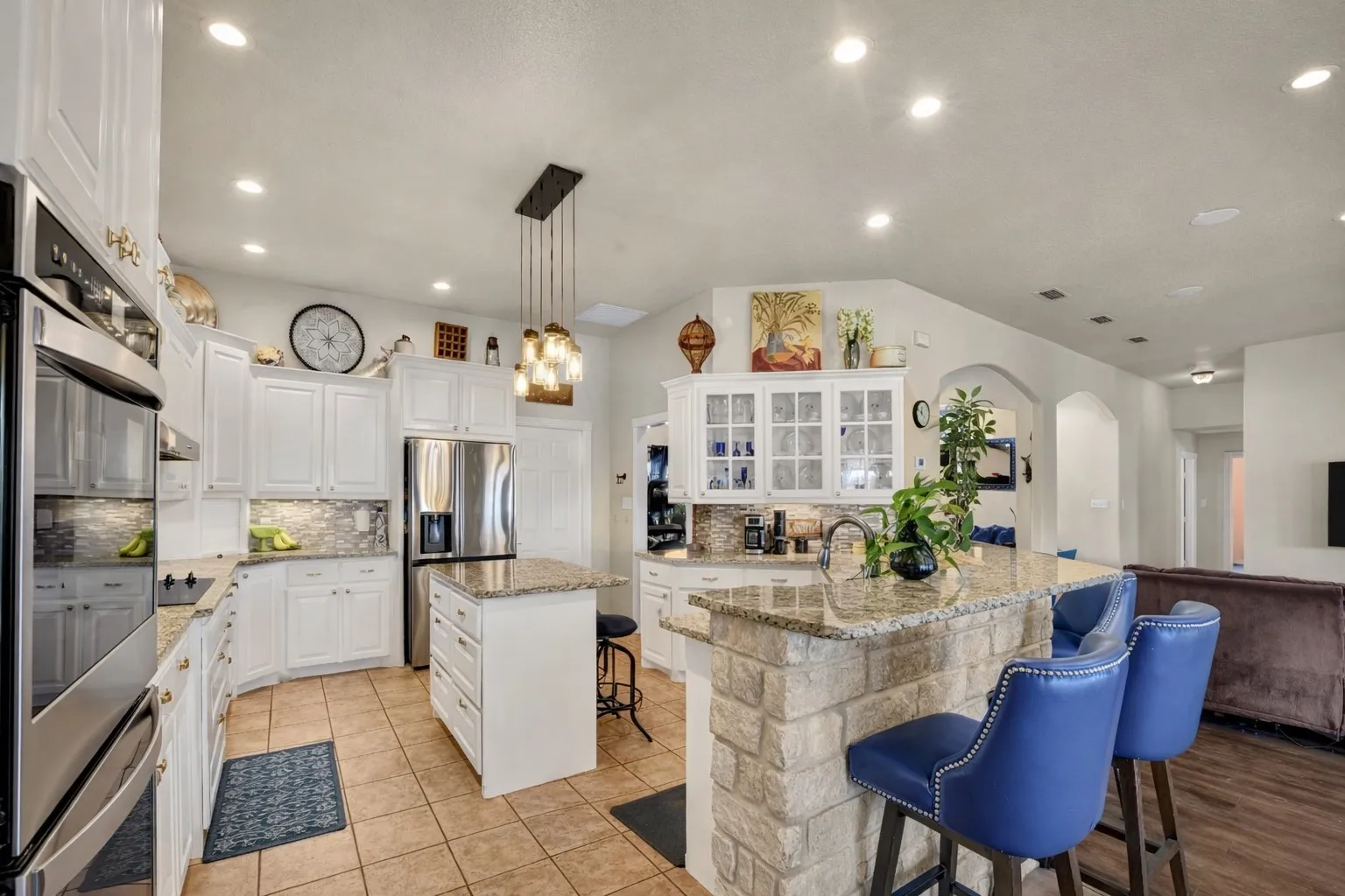 Kitchen featuring tile flooring, white cabinetry, a center island with a granite countertop, stainless steel appliances, and a stone-clad breakfast bar