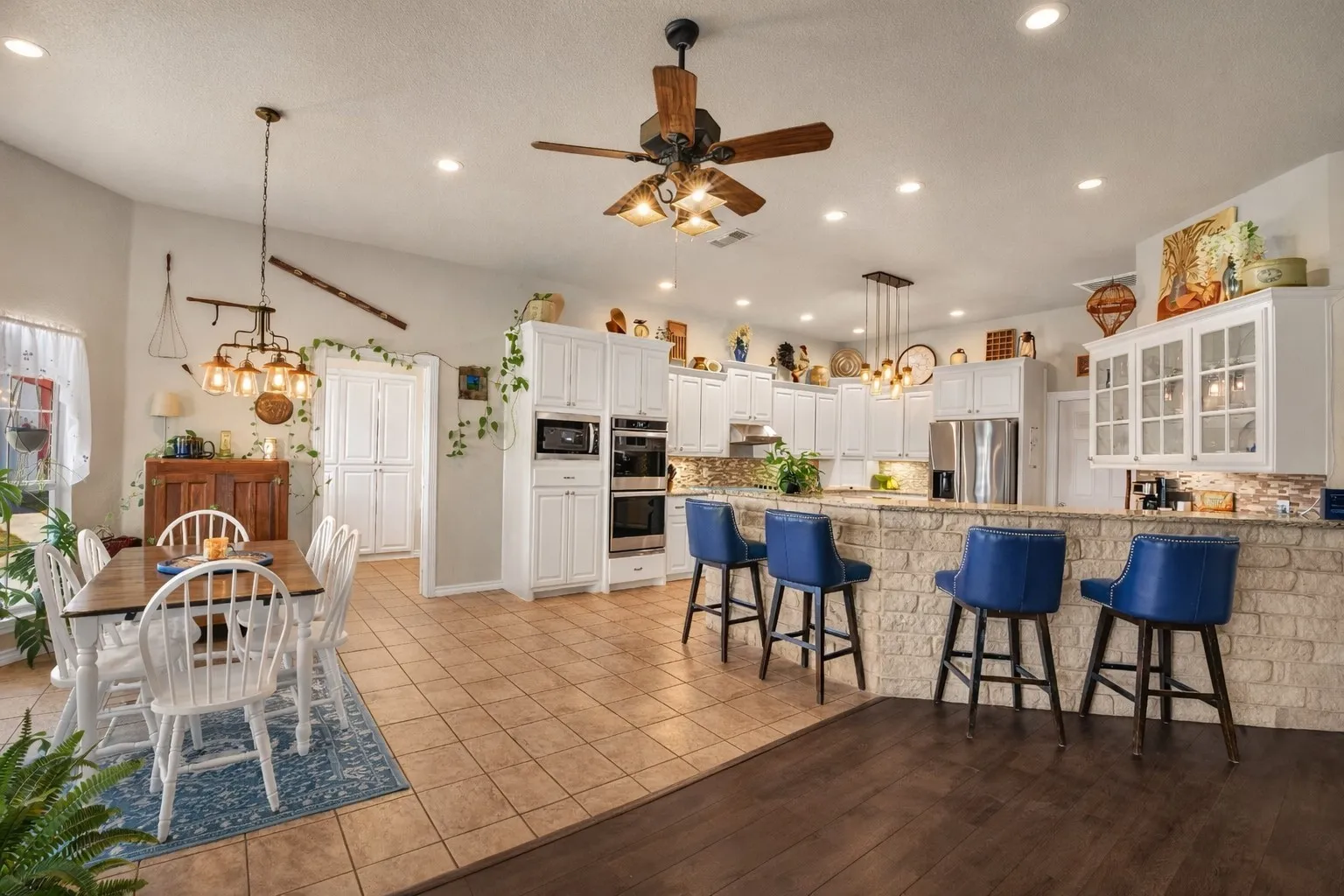 Integrated kitchen and dining area featuring a stone veneer breakfast bar, white cabinetry, recessed lighting, and a wood-finish ceiling fan