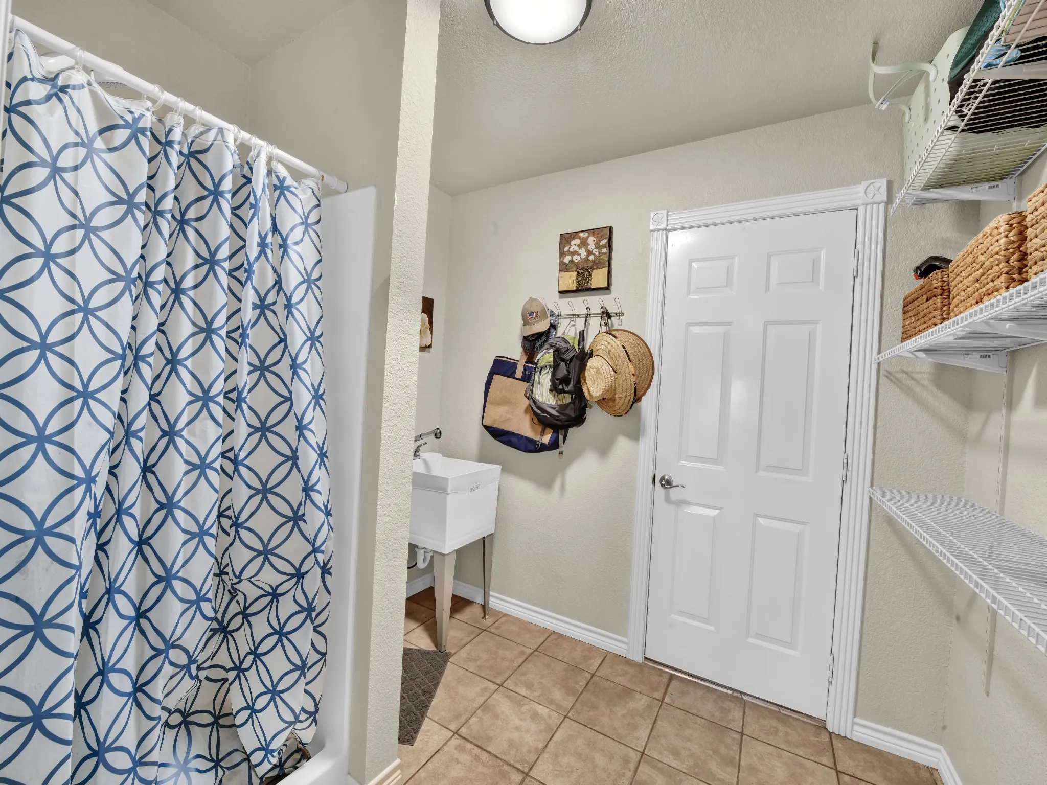 Utility room featuring a built-in sink, tiled flooring, overhead lighting, wire shelving, and a paneled door