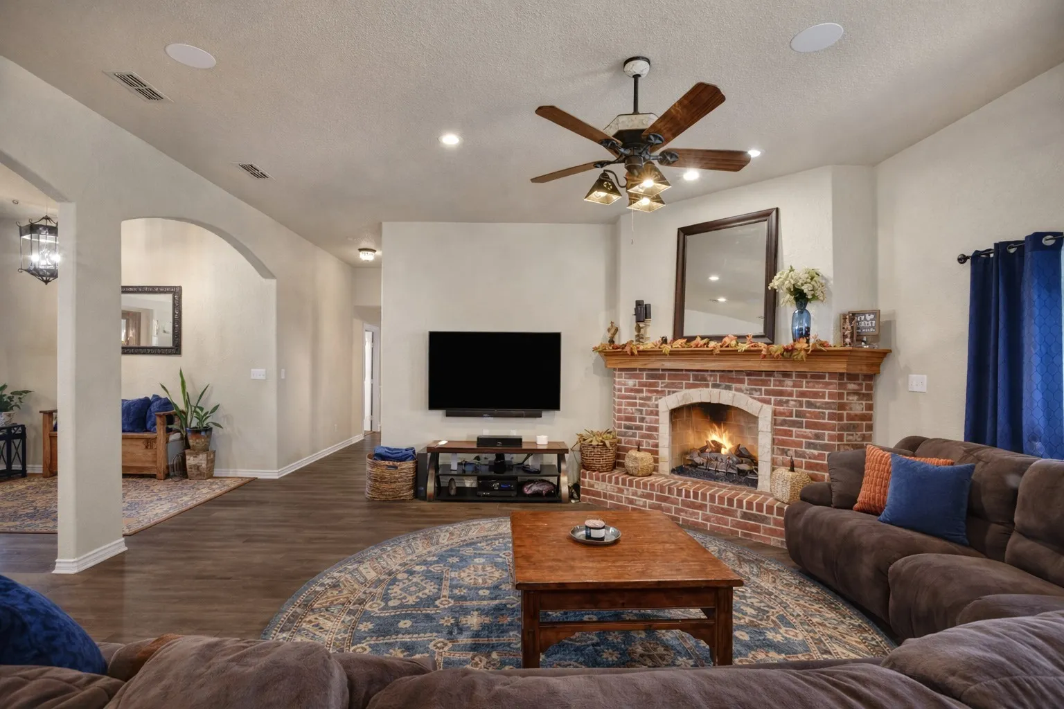 Brick fireplace with a wood mantle, wood-finish flooring, vaulted ceiling, recessed lighting, and an arched doorway