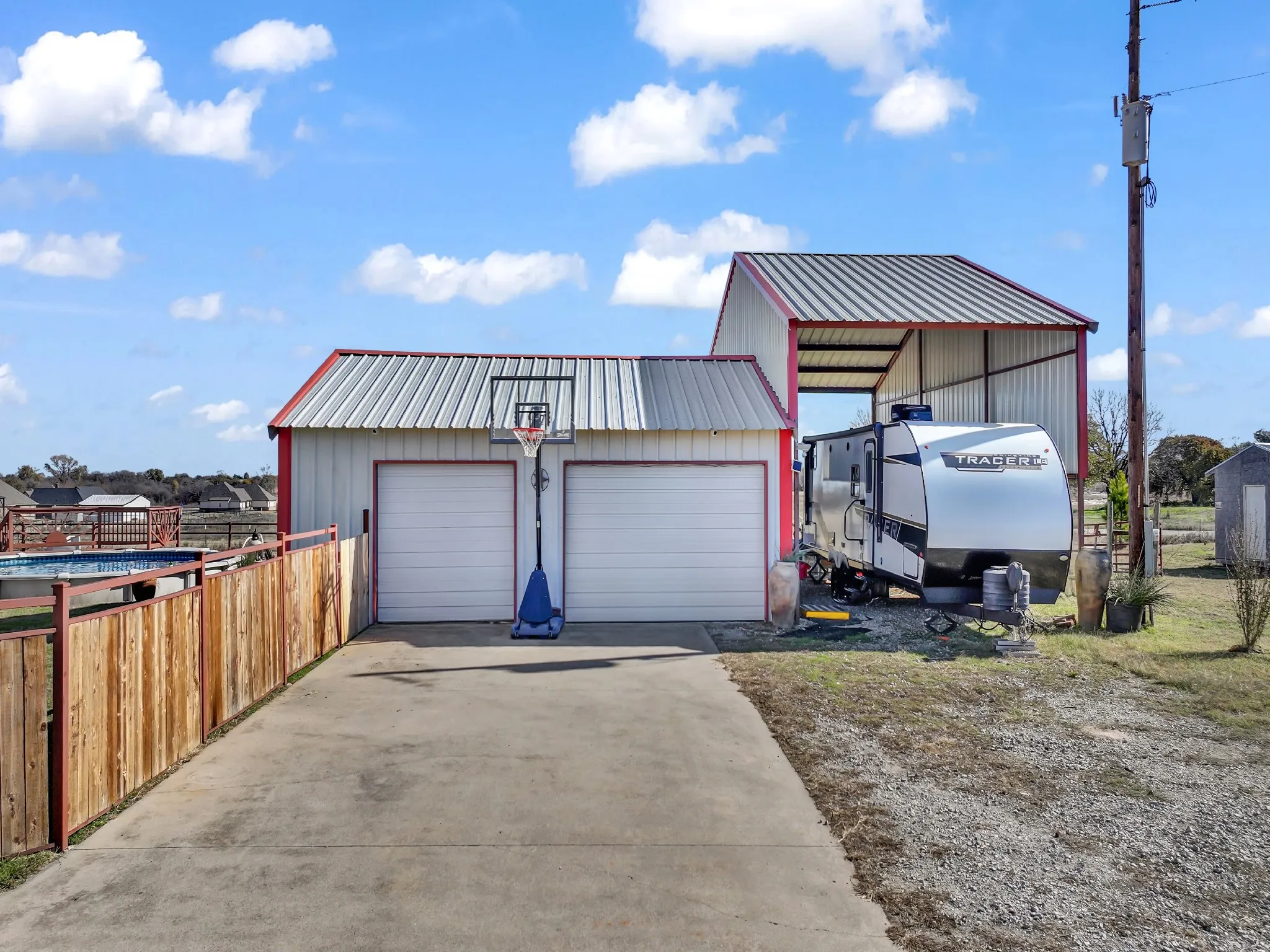 Detached garage structure with two overhead doors, adjacent to a metal-roofed open-sided shed, and a concrete drive