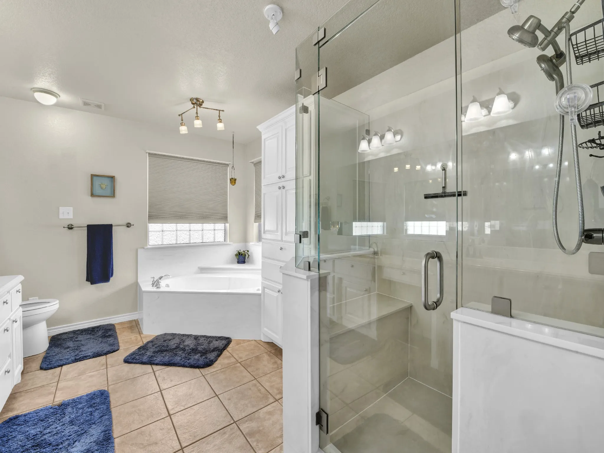 Spacious bathroom featuring a glass-enclosed shower with built-in bench, deep soaking tub, white vanity cabinetry, and tile flooring