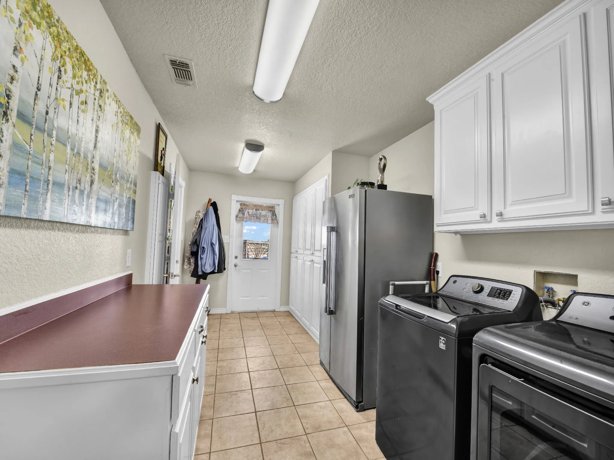 Tile flooring, extensive white cabinetry with crown molding, laminate countertops, and a built-in pantry