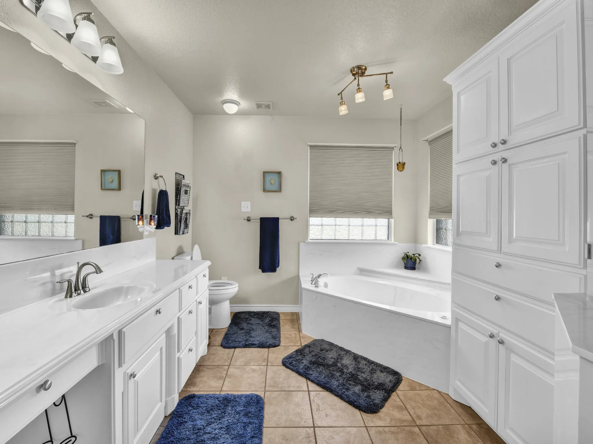 Dual vanity with white cabinetry and integrated sinks, a corner soaking tub, integrated toilet, and extensive built-in white cabinetry