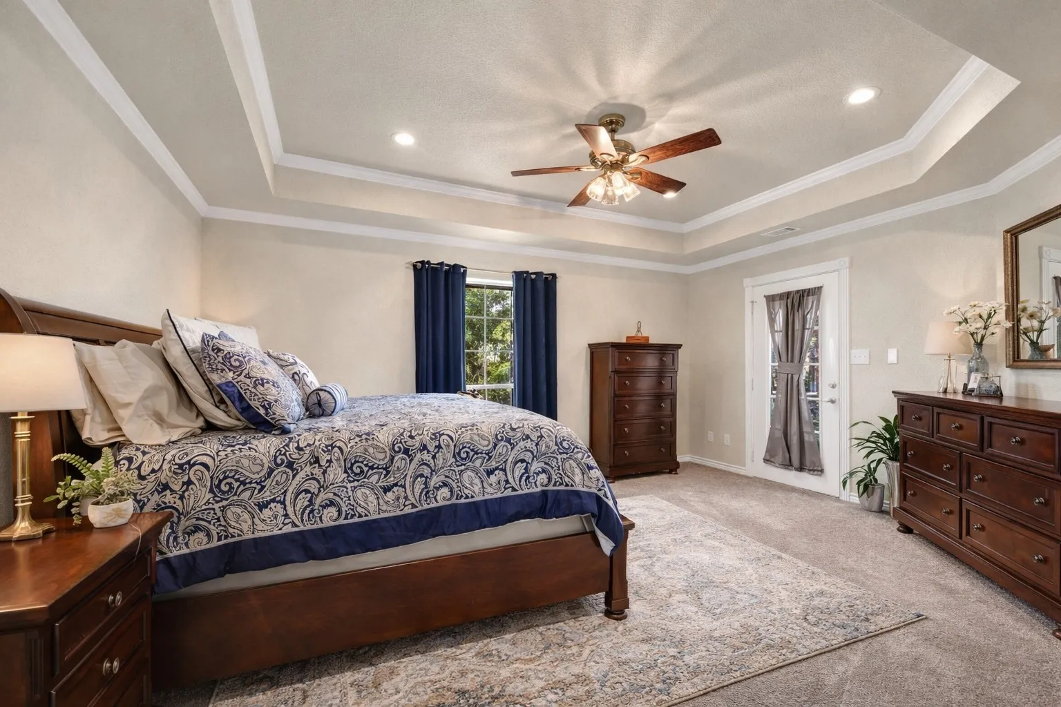 Tray ceiling with crown molding, recessed lighting, ceiling fan, carpeted flooring, and a glass-paned door