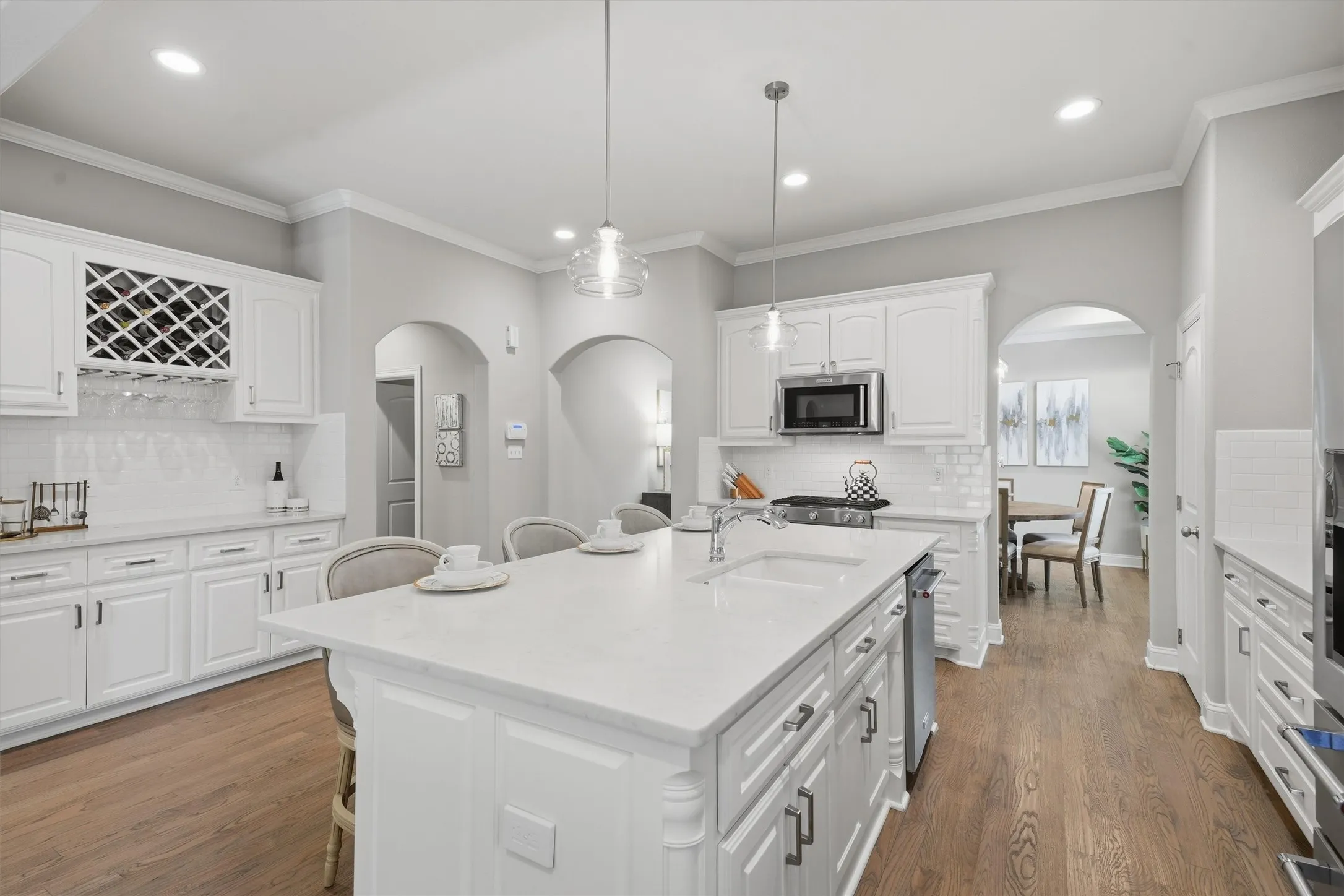 This open kitchen view highlights an oversized island with pendant lighting, bright white cabinetry, and a built-in wine rack. Charming arched doorways seamlessly connect the cooking area to the surrounding dining and living spaces.