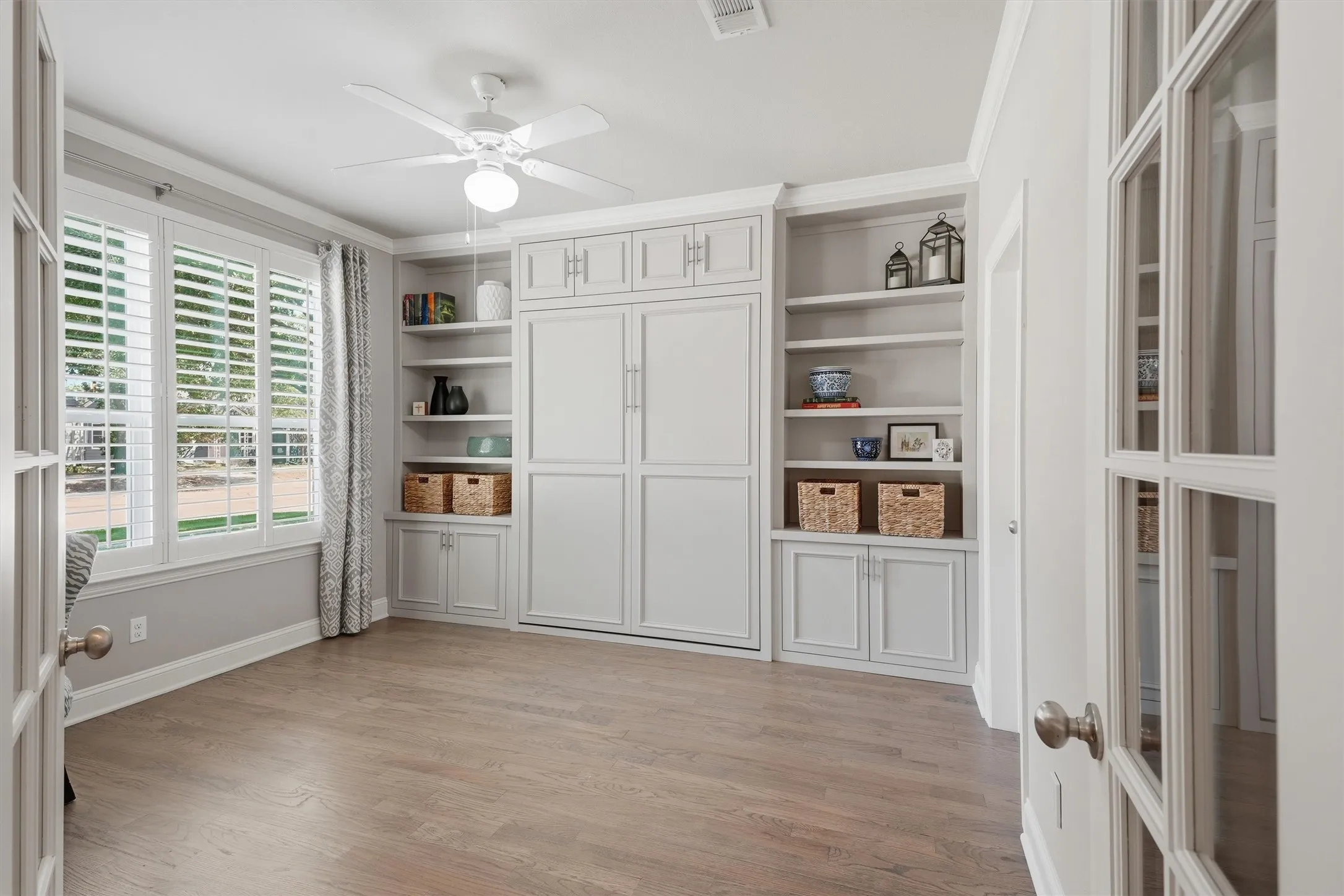 With the Murphy bed stored, this versatile room transforms into an expansive home office or formal study. Glass French doors, plantation shutters, and extensive built-in cabinetry combine function with timeless elegance.