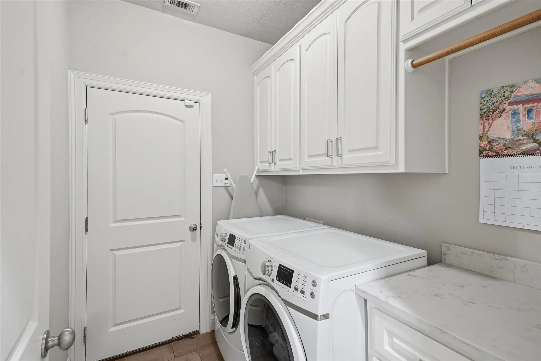 This functional utility room features abundant upper storage cabinets, a dedicated hanging rod, and counter space for folding laundry. Conveniently positioned off the main living spaces, it keeps household chores organized and hidden away.