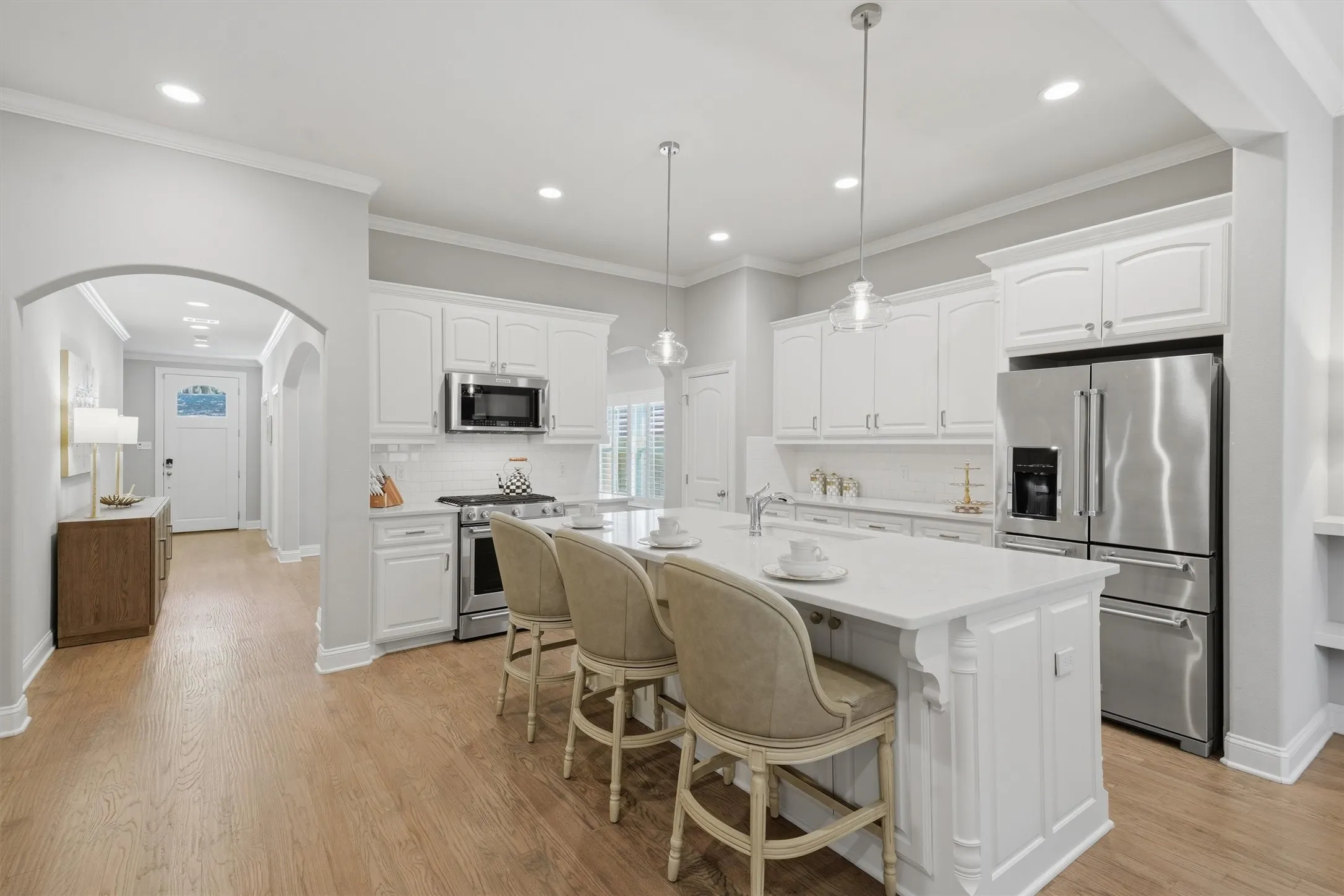 Showcasing a large center island with seating for three and sleek stainless steel appliances. Bright recessed lighting and beautiful wood-look flooring flow effortlessly from the kitchen toward the inviting front entry.