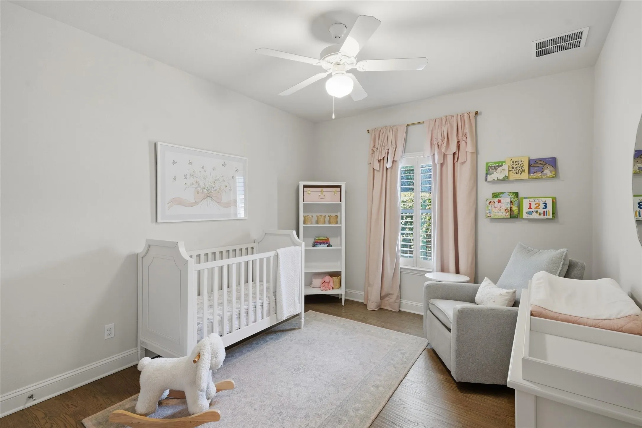 This additional secondary bedroom features clean neutral walls, warm wood flooring, and a ceiling fan. Plantation-shuttered windows fill the comfortable space with natural light, making it ideal for a nursery, kids' room, or guest bedroom.