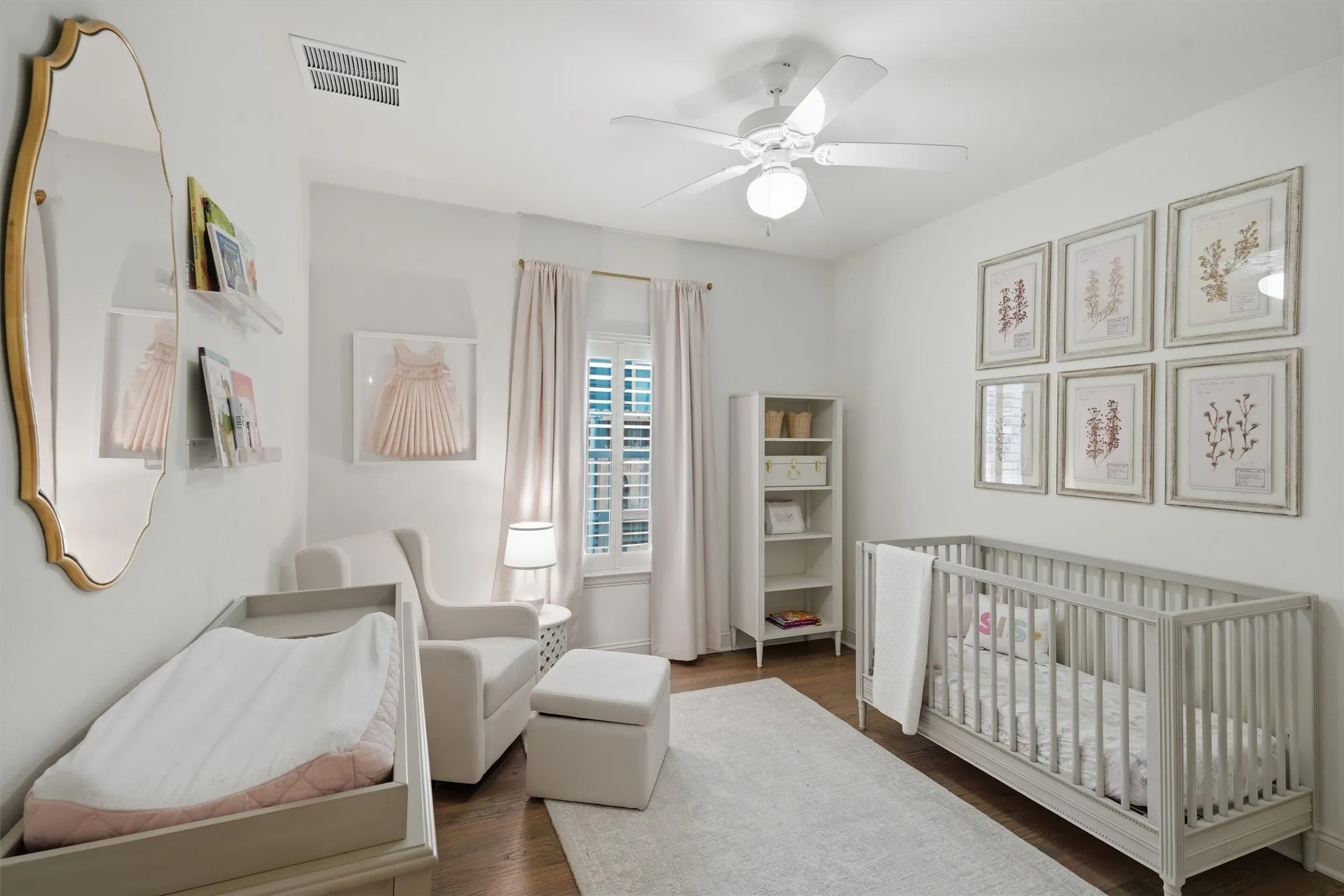 This charming secondary bedroom offers a spacious layout with warm wood flooring and a modern white ceiling fan. Crisp plantation shutters frame the window to let in gentle natural light, creating a bright and cozy retreat.