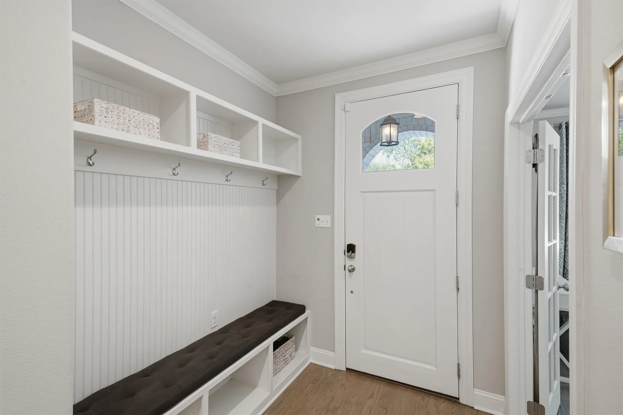 A functional entryway drop-zone features custom built-in cubbies, storage hooks, beadboard accents, and a plush bench seating area. The arched window pane in the front door lets in natural light while maintaining complete privacy.
