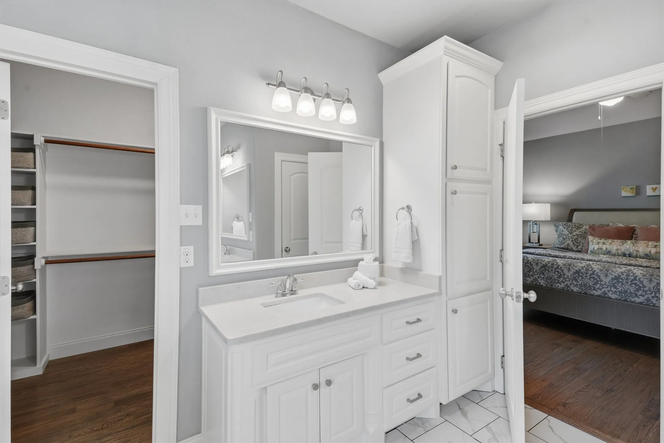 This functional layout highlights a tall built-in linen cabinet alongside a vanity with abundant storage space. Direct access to both the primary bedroom and a spacious walk-in closet with custom shelving makes daily routines effortless.