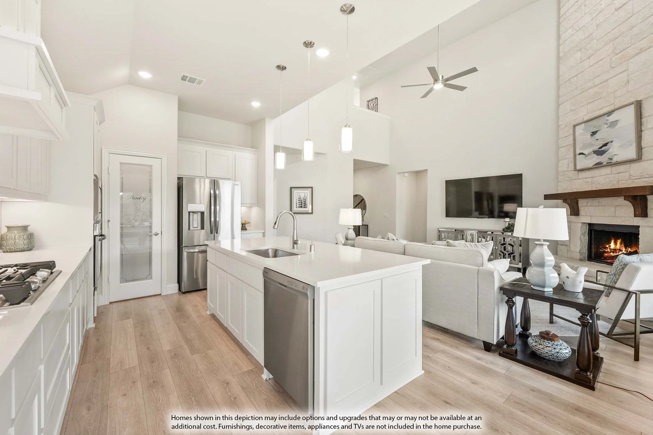 White kitchen cabinetry, stainless steel appliances, central kitchen island with sink, wood-finish flooring, and a stone fireplace with a wood mantel