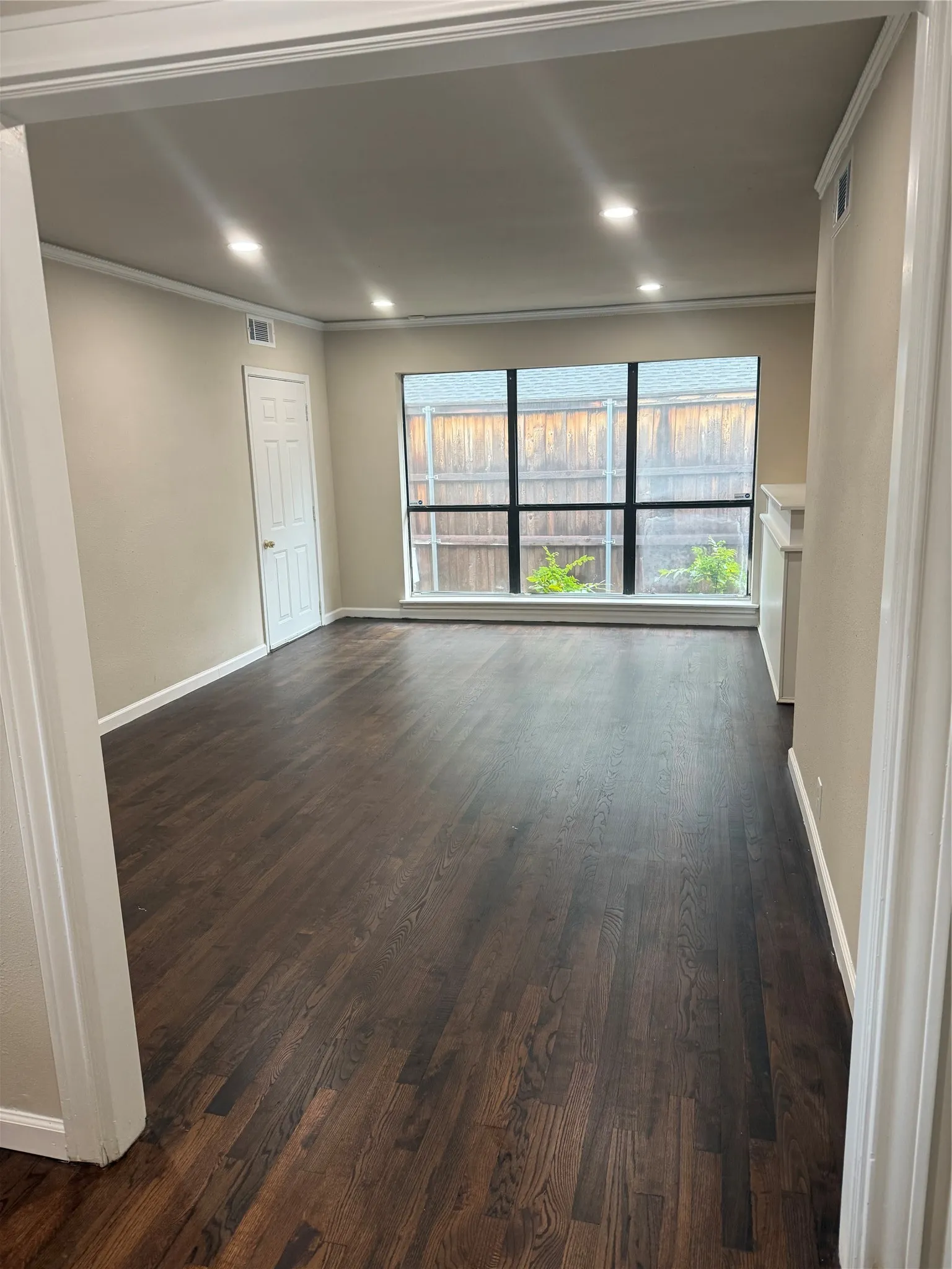 Spacious room featuring dark wood-finish flooring, recessed lighting, and a large multi-pane window