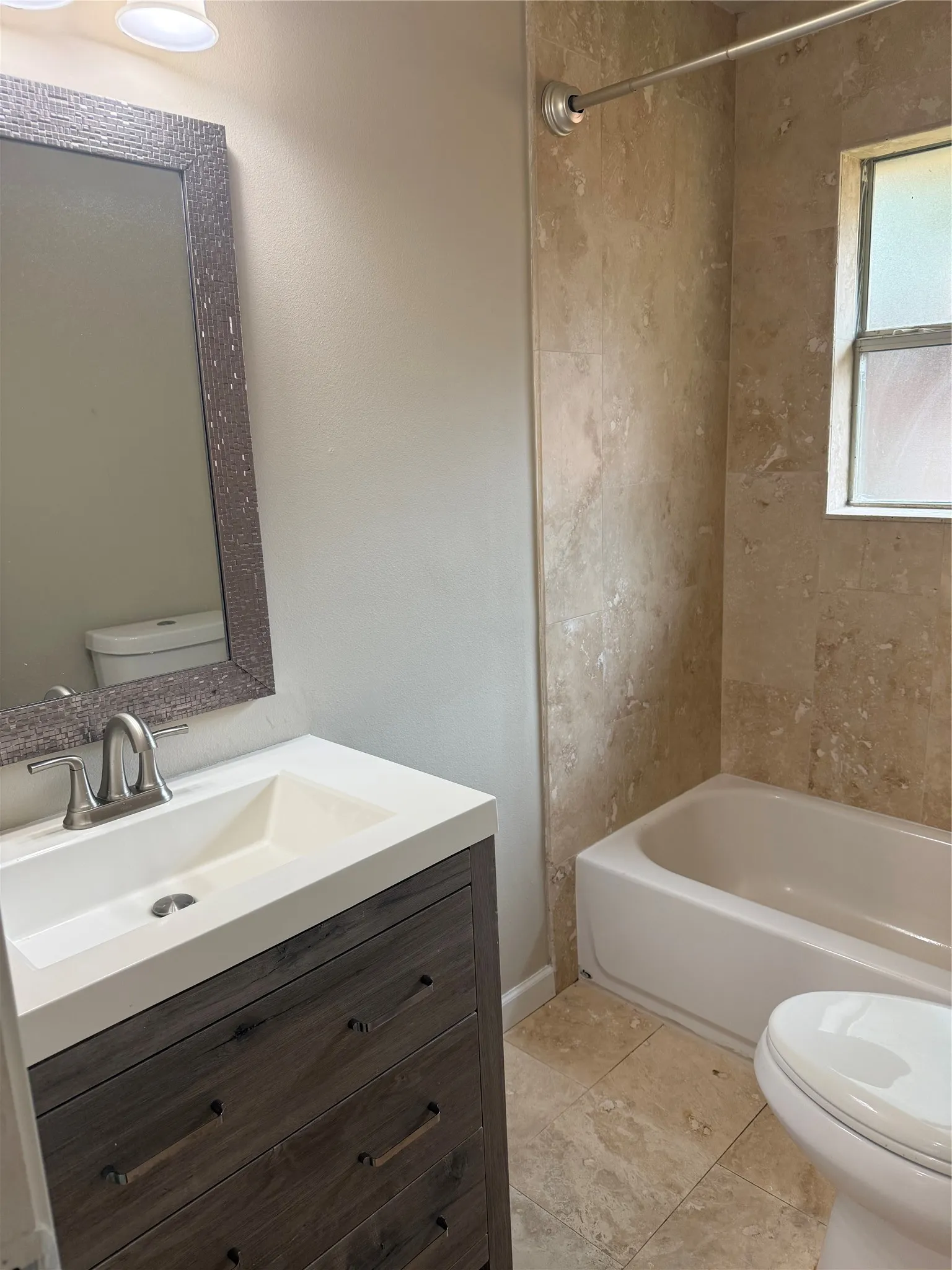 Bathroom featuring a wood-finish vanity with an integrated sink, brushed nickel faucet, tiled shower surround, and tile flooring