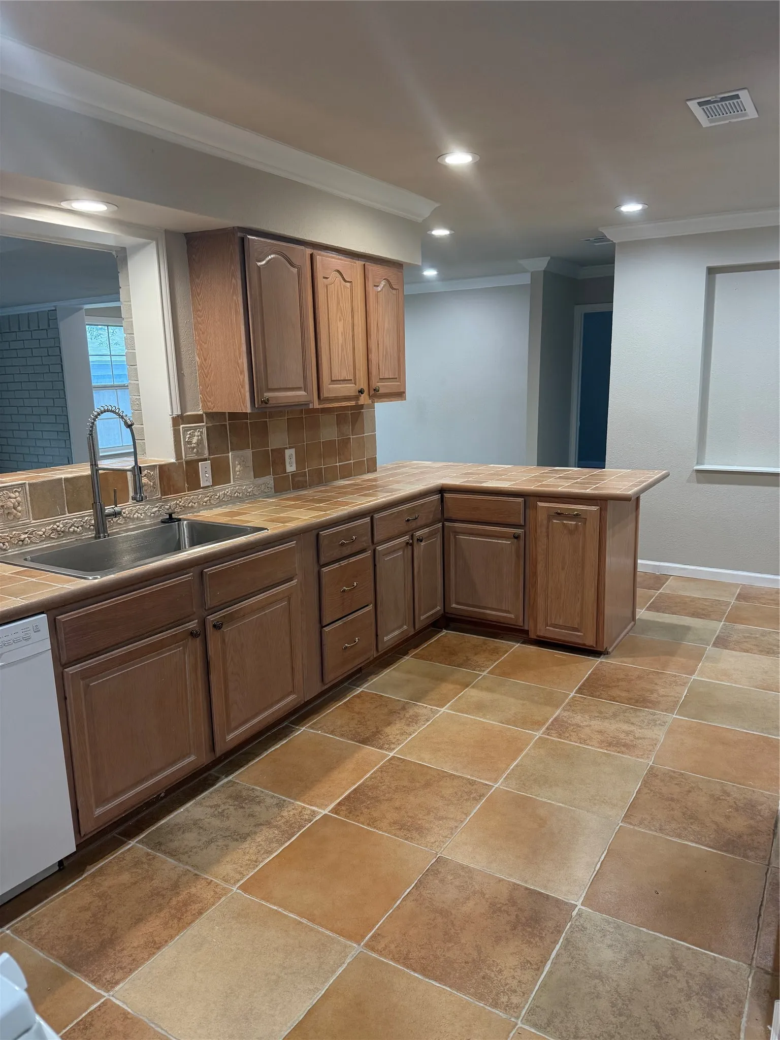 Kitchen featuring wood cabinetry, a stainless steel double basin sink, tile countertops, a tile backsplash, and recessed lighting