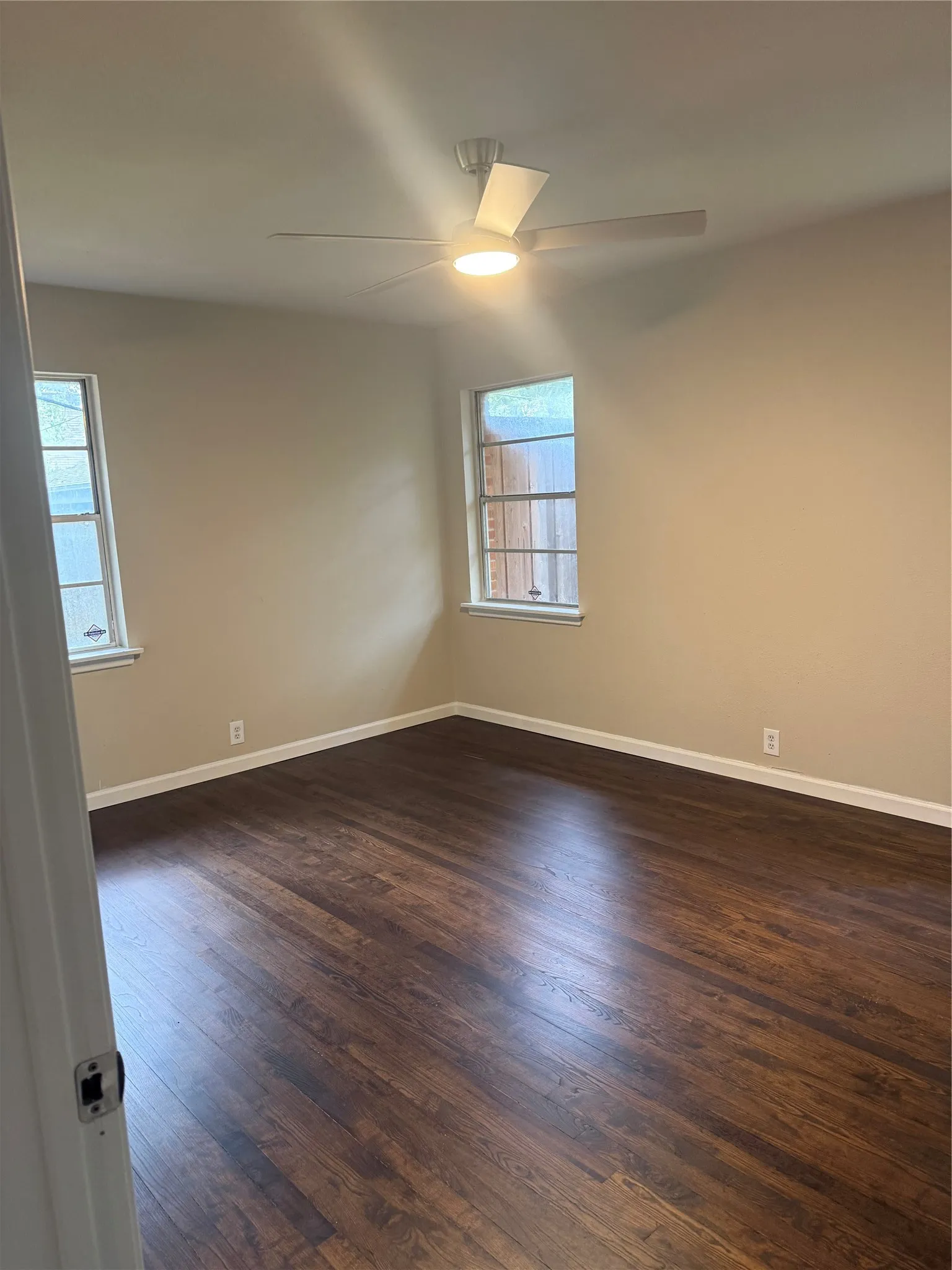 Wood-finish flooring, two windows, and a ceiling fan with integrated lighting