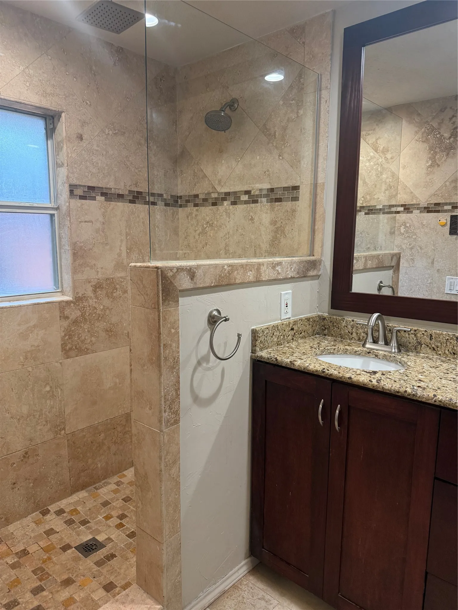 Walk-in shower with natural stone tile, glass enclosure, and a rain showerhead