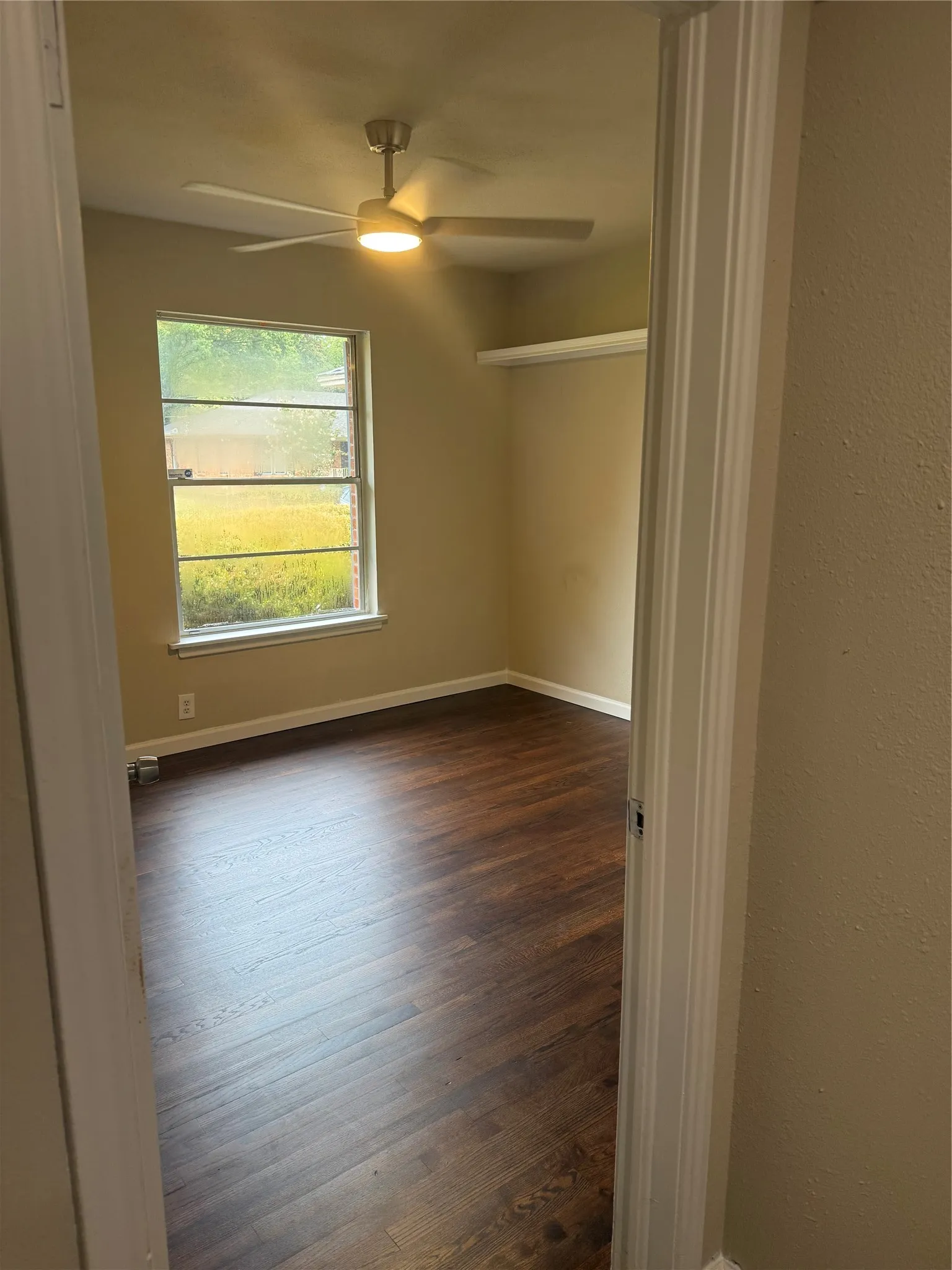 Wood-finish flooring, ceiling fan with integrated lighting, single window, and a built-in wall shelf