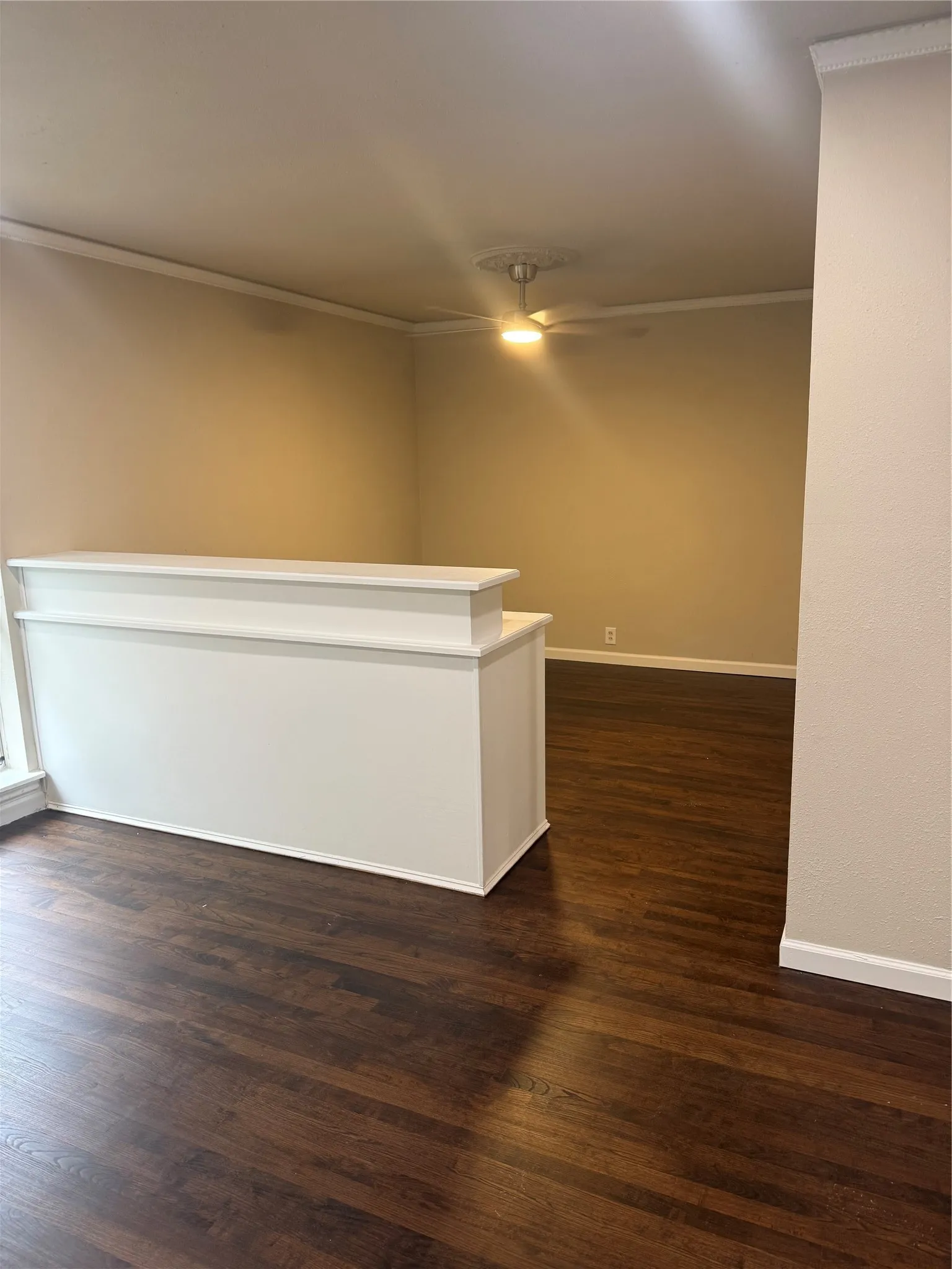 Dark wood-finish flooring, half-wall partition, crown molding, and a ceiling fan with light
