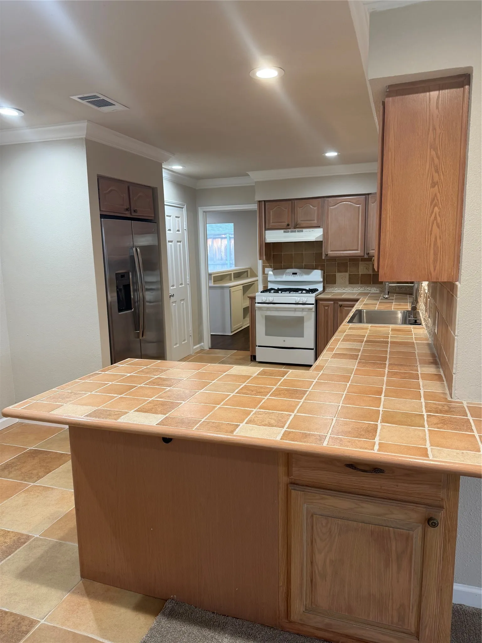 Kitchen featuring a stainless steel refrigerator, white gas range, wood cabinetry, tile countertops, and recessed lighting