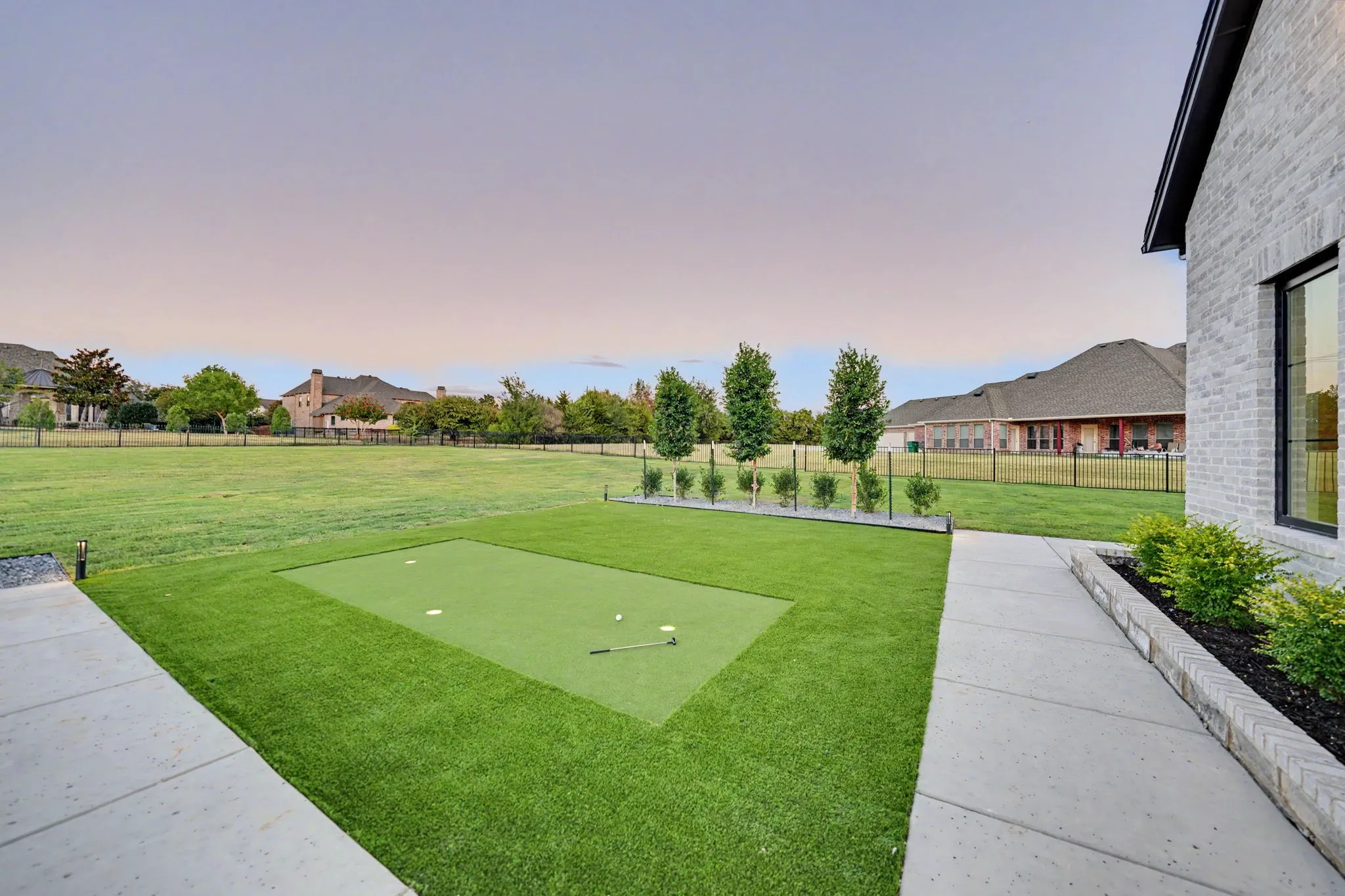 Expansive green space featuring a built-in putting green, concrete pathway, and a brick-faced exterior