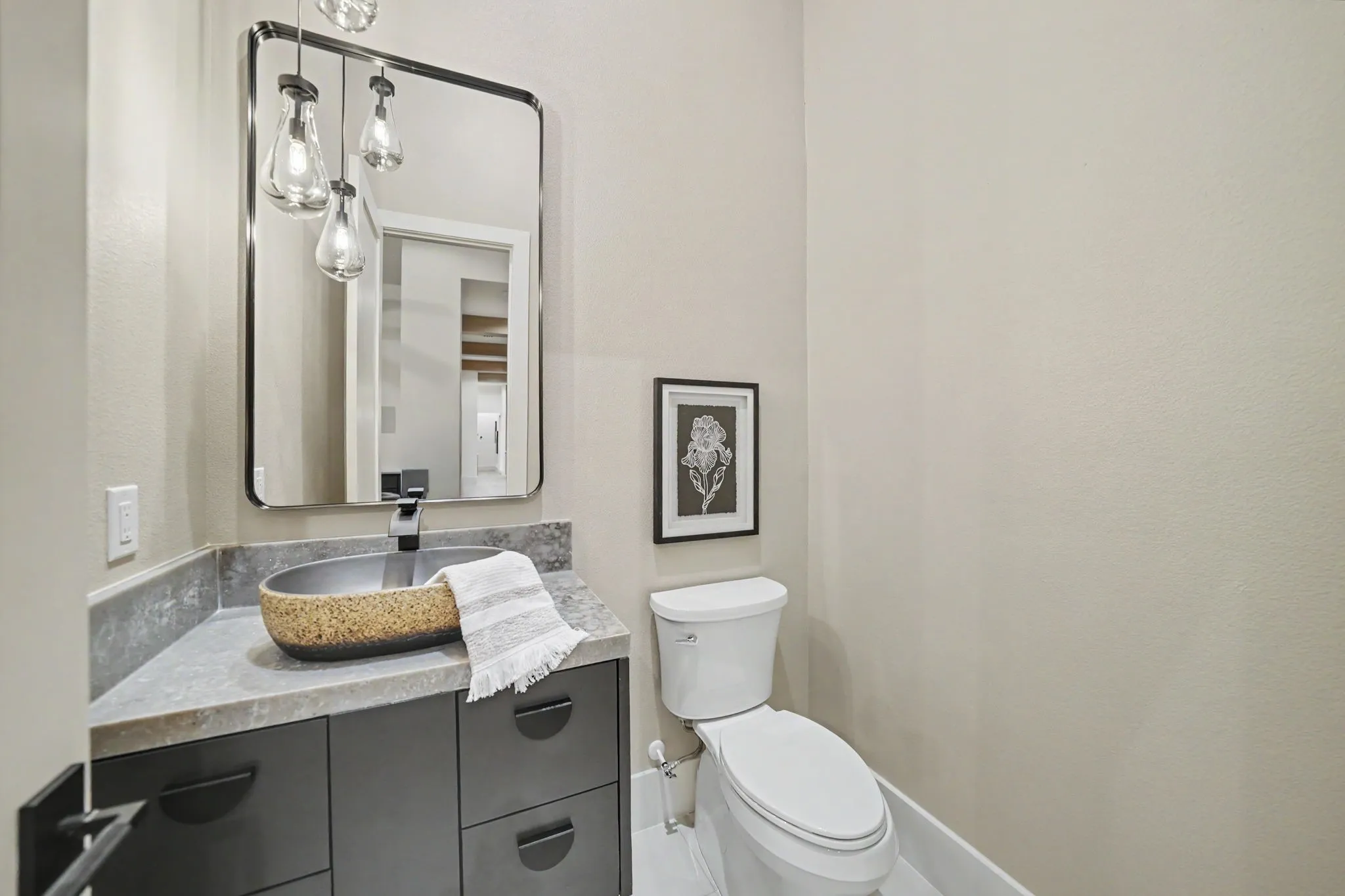 Bathroom featuring a dark gray vanity with contemporary hardware, a vessel sink with a unique textured exterior, a dark gray countertop, a rectangular mirror, and a multi-light pendant fixture