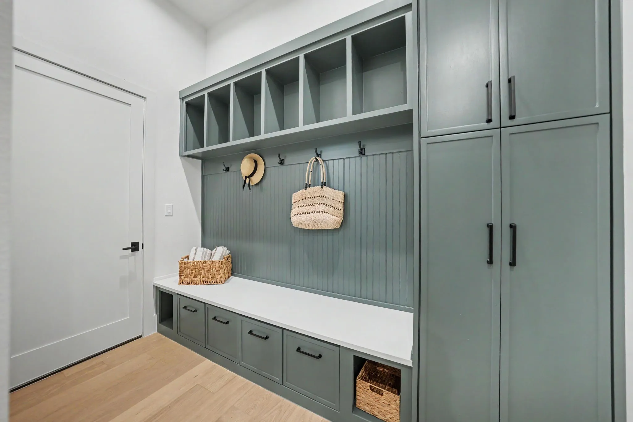 Built-in cabinetry with open cubbies, beadboard paneling, integrated bench seating, and wood-finish flooring