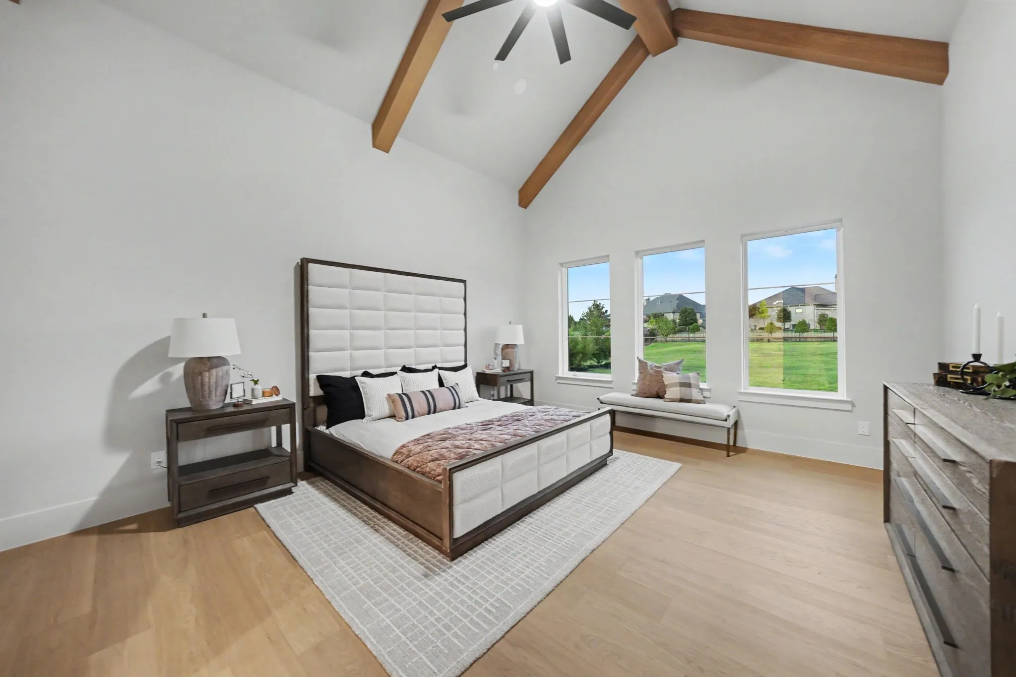 Vaulted ceiling with exposed wood beams, overhead ceiling fan, light wood-finish flooring, and multiple windows