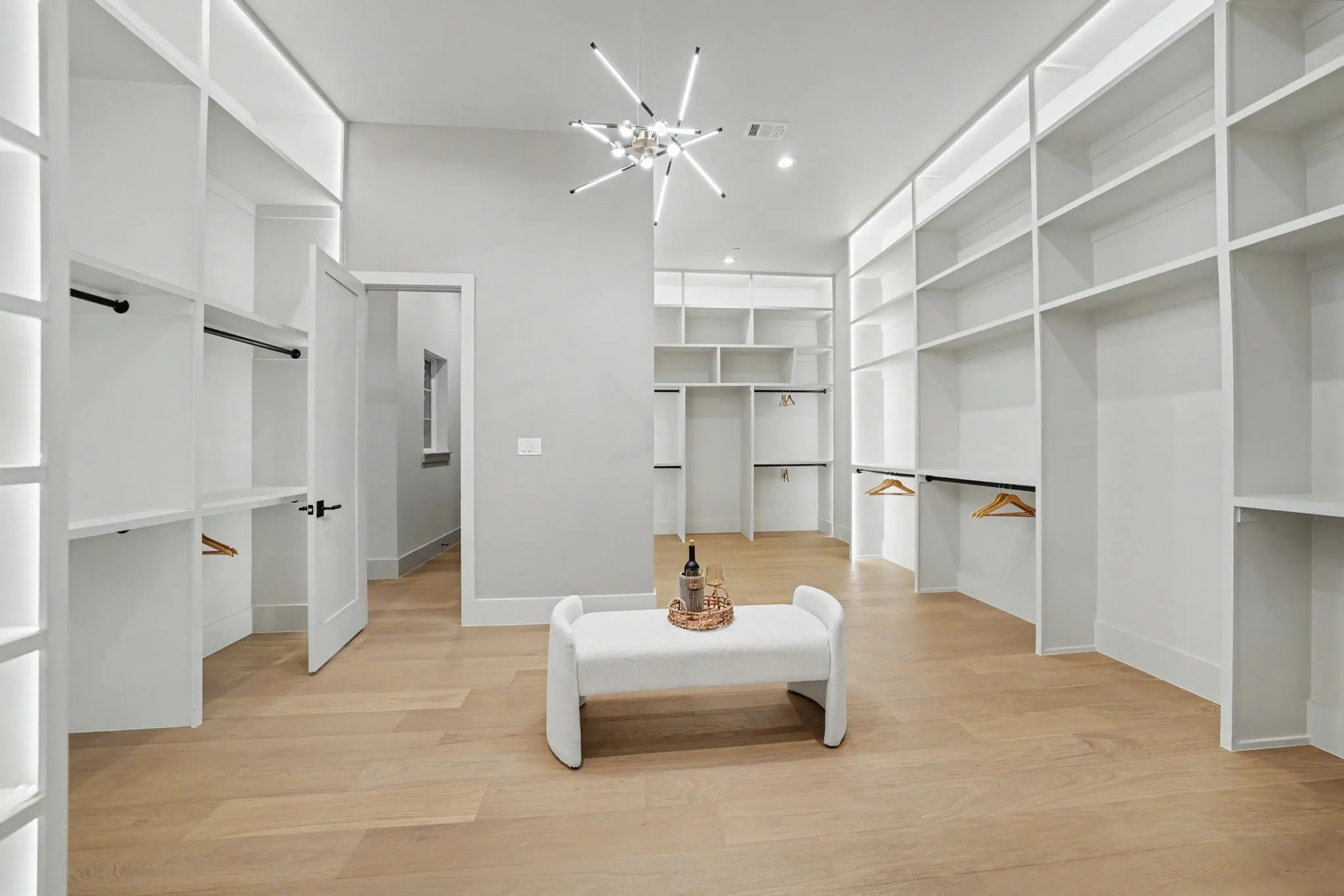 Expansive walk-in closet featuring extensive built-in shelving, integrated lighting, wood-finish flooring, and a modern ceiling fixture