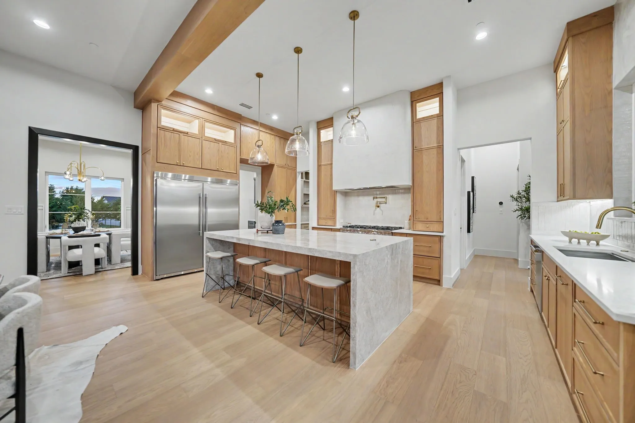 Spacious kitchen featuring light wood-finish flooring, a large waterfall island with integrated seating, extensive wood cabinetry, and stainless steel built-in appliances