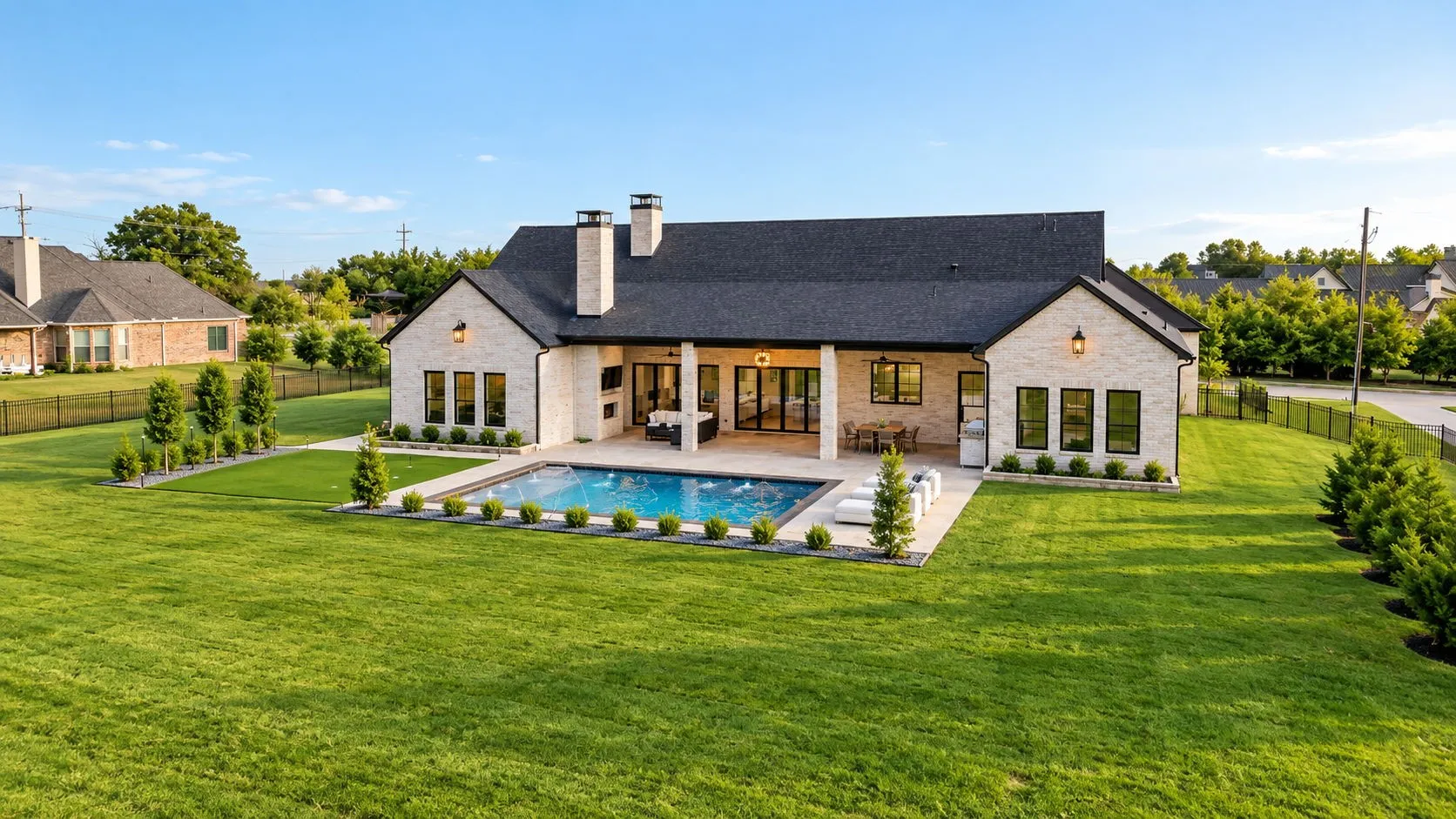 Limestone-style exterior with a dark shingle roof, featuring an outdoor swimming pool, covered patio, and extensive lawn space