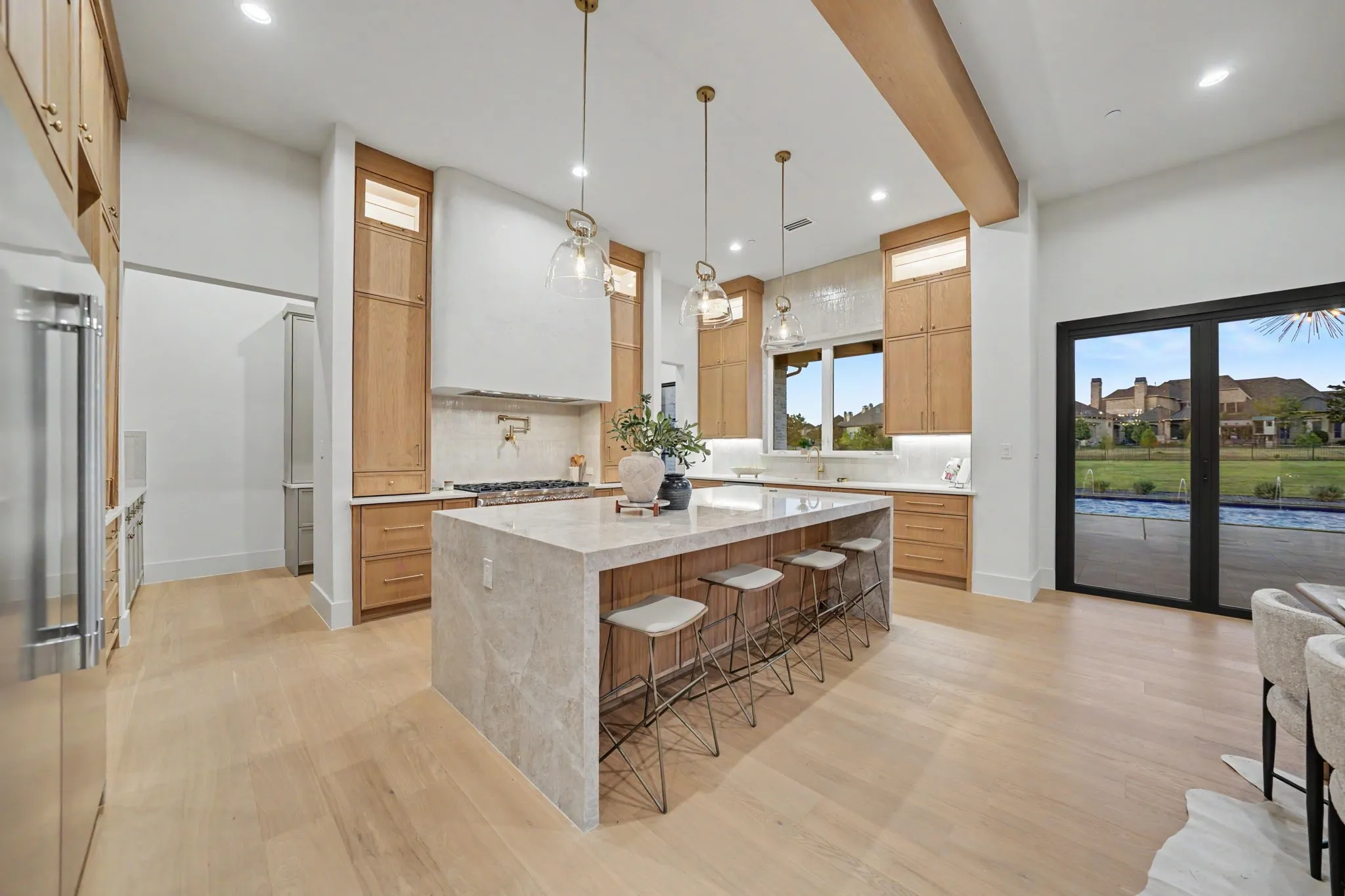 Spacious kitchen featuring wood-finish cabinetry, a large waterfall island, light-toned wood-finish flooring, and recessed lighting