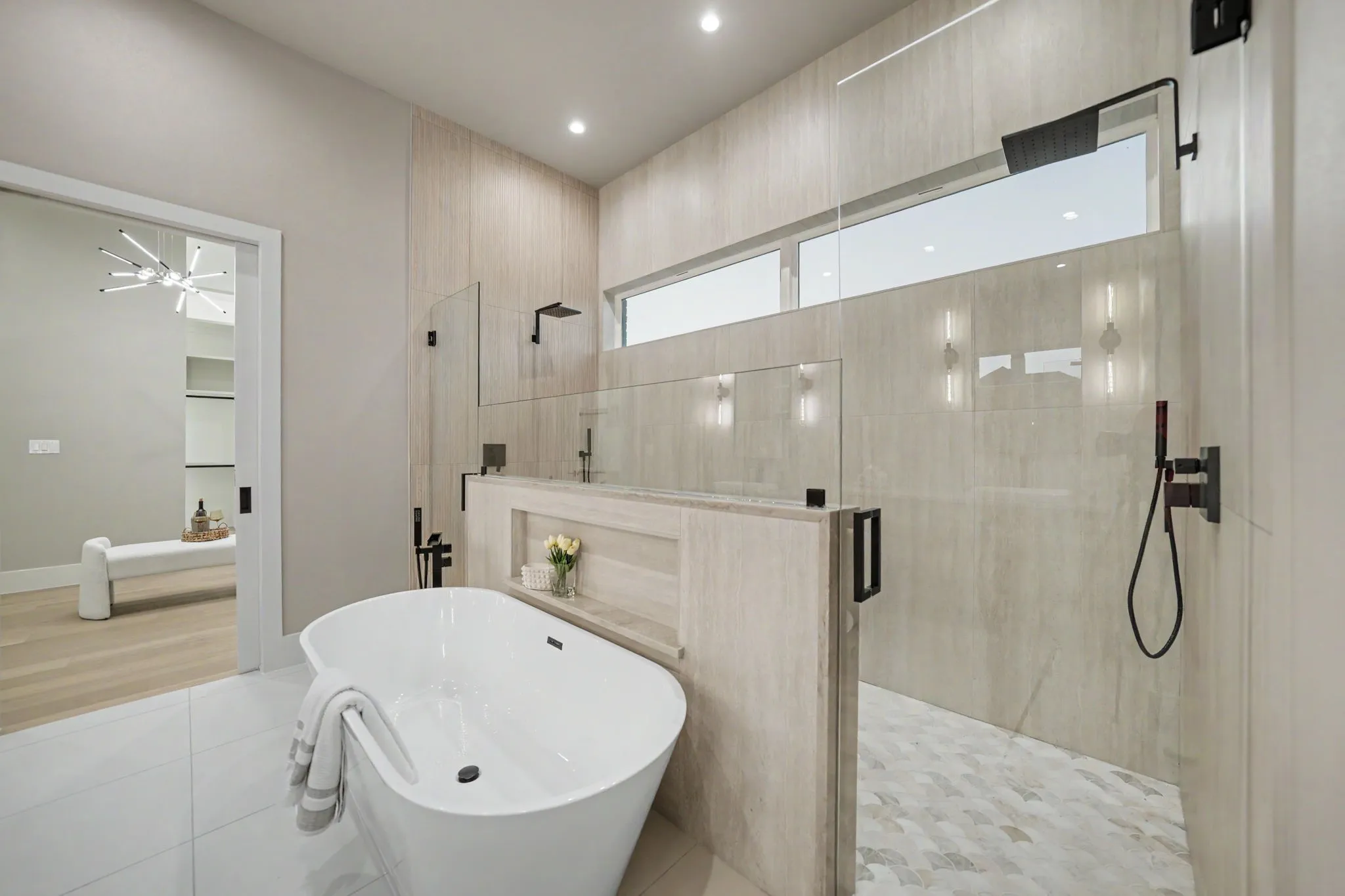 Freestanding soaking tub with a built-in shelf, glass-enclosed shower, transom window, and matte black fixtures